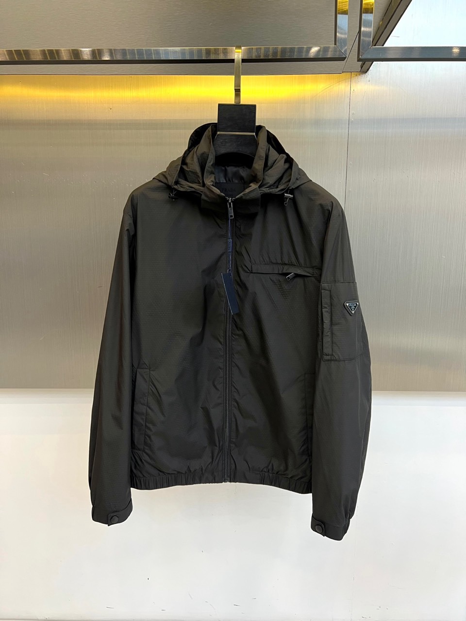 NO:760798,Prad, the new men's hooded jacket for spring and summer 2026, reshapes urban outdoor style with minimalist workwear aesthetics. The color is calm and versatile, suitable for multiple scenarios such as commuting, hiking, and city roaming. It is made of high-density windproof fabric, which is light, flexible, anti-wrinkle and easy to care for, and has a slightly breathable inner knot.  The structure ensures physical comfort under the temperature difference between spring and summer. The three-dimensional tailoring fits the body shape but is not restrictive. The hooded design is equipped with an adjustable drawstring, taking into account both style and practicality; the front full zipper opening and closing is neat and capable, the three-dimensional patch pockets on the chest enhance the sense of functionality, and the side zipper pockets on the sleeves take into account storage and safety; the triangle logo point on the left arm  Eye-catching brand recognition, low-key and unobtrusive. The hem and cuffs are elasticated to prevent wind and temperature while maintaining a neat silhouette. The overall style combines modern urban functionality and outdoor pragmatism. It is a must-have item in the 2026 spring and summer wardrobe that is both functional and fashionable, whether it is worn with casual wear or not.  Wear casual pants to create a relaxed Japanese style, or layer a shirt for a light business look. You can handle it all with ease, highlighting contemporary men's dual pursuit of quality and style. 48-56 (model weighs 173,143 pounds, upper body size 50),, prada, prada, jackets  & coats,shirts,hats,19860909Prad普拉达、2026春夏新品男士连帽夹克,以极简工装美学重塑都市户外风格,色调沉稳百搭,适配通勤、徒步、城市漫游等多重场景.采用高密度防风面料,轻盈柔韧且抗皱易打理,内里微透气结构确保春夏温差下的体感舒适.立体剪裁贴合身形却不束缚,连帽设计配可调节抽绳,兼顾造型与实用性；正面全拉链开合利落干练,胸前立体贴袋强化机能感,袖侧拉链口袋兼顾收纳与安全；左臂三角徽标点睛品牌辨识度,低调不张扬.下摆与袖口均采用松紧收束设计,防风锁温同时保持利落轮廓.整体风格融合现代都市机能与户外实用主义,是2026春夏衣橱中兼具功能性与时尚感的必备单品,无论是搭配休闲裤打造日系松弛感,还是叠穿衬衫演绎轻商务造型,皆能从容应对,彰显当代男性对品质与风格的双重追求.48-56（模特173,143斤上身50码）,,prada,prada,jackets & coats,shirts,hats,,Men's clothing