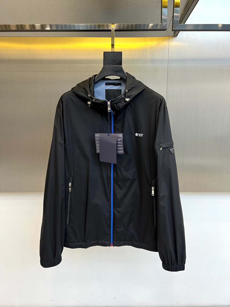 NO:760812,Prada, the new hooded jacket for spring and summer 2026, reshapes urban outdoor aesthetics with avant-garde functional style. The main theme is matched with eye-catching zippers. The contrasting color design breaks the dullness and has both recognition and visual tension. Lightweight nylon fabric (polyamide) gives the clothing excellent wind resistance and breathability.  , suitable for various scenes such as spring weather, summer commuting, and outdoor exploration. The hooded structure is equipped with a metal adjustment buckle, which can be adjusted according to needs to enhance practicality; zipper pockets on both sides ensure safe storage, and the brand triangle logo on the sleeves echoes the small logo on the chest, low-key highlighting the luxury brand founda19860909Prad普拉达、2026春夏新品连帽夹克,以先锋机能风重塑都市户外美学,主调搭配亮眼拉链,撞色设计打破沉闷,兼具辨识度与视觉张力.轻量化尼龙面料（聚酰胺）赋予服装卓越防风性与透气感,适合春日多变天气与夏季通勤、户外探索等多元场景.连帽结构搭配金属调节扣,可根据需求调整松紧,增强实用性；两侧拉链口袋保障收纳安全,袖部品牌三角标与胸前小logo呼应,低调彰显奢牌基因.内衬采用棉质非纺织动物源成分,亲肤舒适,洗涤标签清晰标注专业护理方式,确保衣物持久挺括.整体剪裁利落,收口袖口与下摆优化身形比例,既保有运动装的活力动感,又融入高级时装的设计语言,是都市精英型格与户外机能风的完美融合,轻松驾驭街头潮流与日常通勤,开启春夏穿搭的质感新纪元.48-56（模特173,143斤上身50码）,,prada,prada,jackets & coats,hats,,Men's clothing