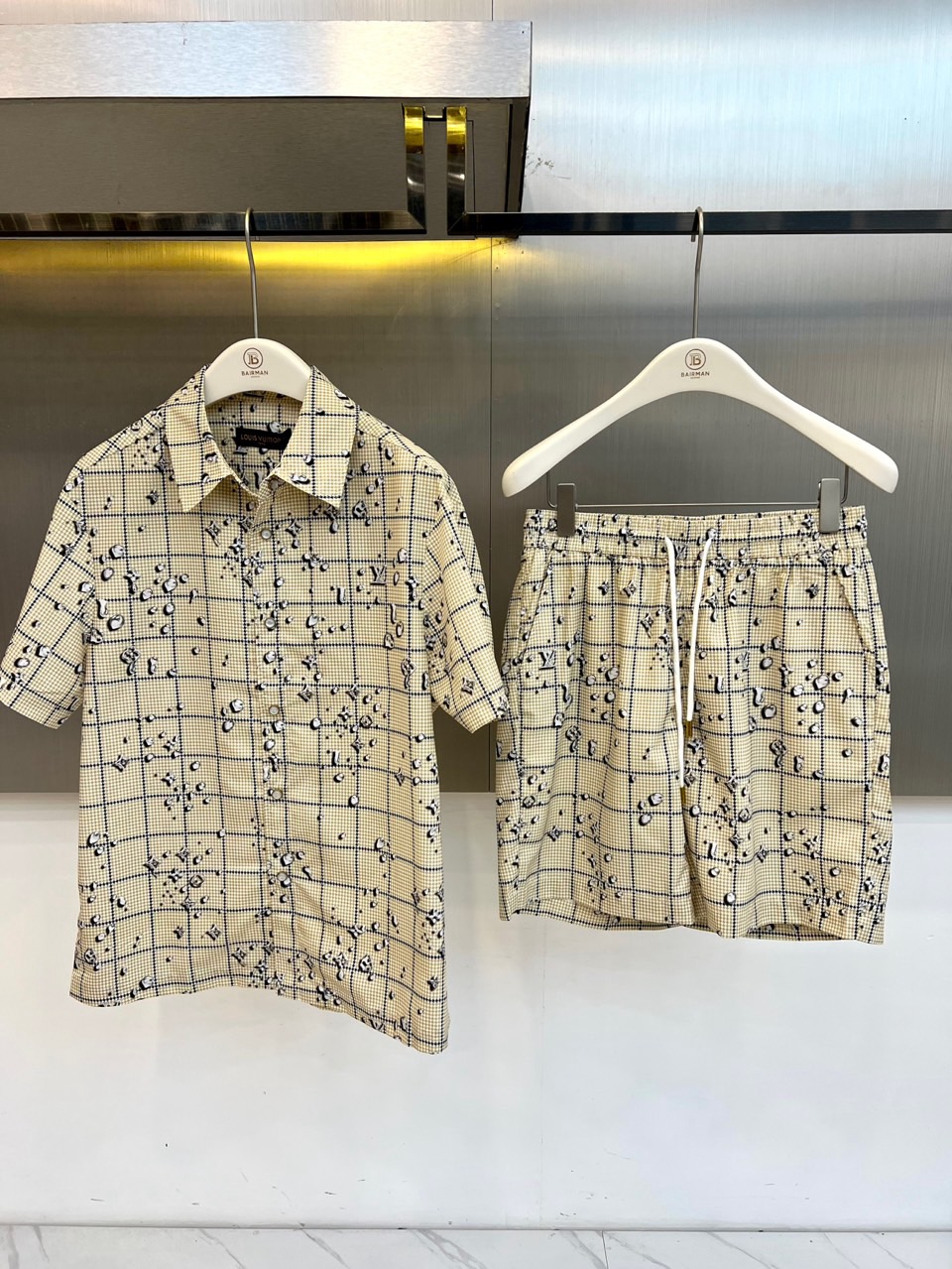 NO:840815,One set.  1v Vuitton, 2026 spring and summer new suit, based on classic plaid, cleverly integrates three-dimensional beads and brand logo elements, interpreting the exquisite casual style of the modern city. The short-sleeved shirt is crisply cut, the lapel design is matched with front buttons, and the details are embellished with beads like stars, giving it a basic foundation  The plaid pattern has a smart and layered feel; the shorts echo the same, the elastic waistband is adjustable with a drawstring, and it fits comfortably to the body shape; the side pockets are practical and stylish, and the beads and plaid patterns are intertwined to continue the overall visual rhythm. The whole set is made of light and breathable fabrics, adapting to the changing climate of spring and summer, and meeting the decent needs of commuting occasions  , it is also suitable for relaxed scenes such as weekend outings and coffee shop breaks. The plaid pattern is low-key but not out of style, and the beads brighten it to break up the dullness, highlighting the low-key luxury aesthetic taste. The brand logo is cleverly integrated into the design, not overpowering the guest but hiding the identity mark. In the spring and summer of 2026, the classic plaid is reborn, with fine details  Interpreting a sense of luxury, this suit is both practical and aesthetic. It is an indispensable trendy choice in your wardrobe. You can easily wear it to make your own fashion statement. 48-56 (model weighs 173,143 pounds, upper body size 50), shorts, shirts, T-shirt,19860909一套. 1v威登、2026春夏新品套装,以经典格纹为基底,巧妙融入立体珠饰与品牌标识元素,演绎现代都市的精致休闲风.短袖衬衫采用挺括剪裁,翻领设计搭配前襟纽扣,细节处珠饰点缀如星河洒落,赋予基础格纹灵动层次感；短裤同步呼应,松紧腰头配抽绳调节,舒适贴合身形,侧边口袋实用兼具造型感,珠饰与格纹交织,延续整体视觉韵律.整套选用轻盈透气面料,适应春夏多变气候,既满足通勤场合的得体需求,亦适配周末出游、咖啡厅小憩等轻松场景.格纹低调不失格调,珠饰提亮打破沉闷,彰显低调奢华的审美品味.品牌标识巧妙融入设计,不喧宾夺主却暗藏身份印记.2026春夏,让经典格纹焕发新生,用细节诠释高级感,这套兼具实穿与美学的套装,是你衣橱中不可或缺的潮流之选,轻松穿出属于你的时髦宣言.48-56（模特173,143斤上身50码）,,shorts,shirts,T-shirt,,Men's clothing
