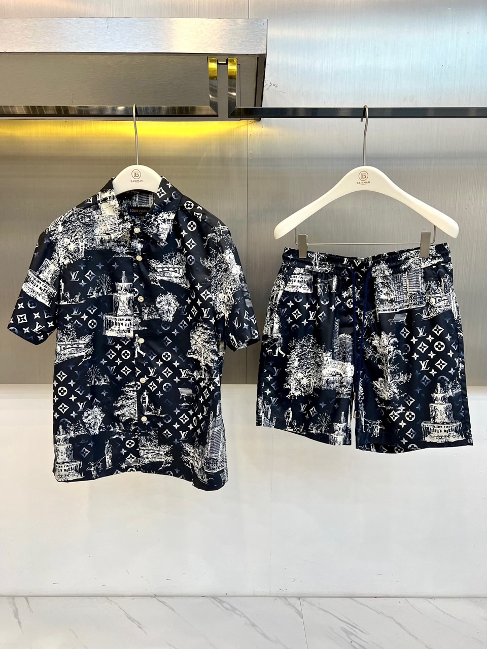 NO:840811,One set.  1v Vuitton, 2026 spring and summer new product suit, reconstructs the classic logo with artistic touches to create a fashionable item that combines vacation relaxation with urban luxury style. The short-sleeved shirt adopts a loose silhouette, crisp lapels and neat plackets, and is full of hand-painted urban buildings, natural scenery and brand symbols.  Numbers are intertwined, and the lines burst out retro literary tension on the background. The fabric is breathable and draped, suitable for strolling on a sunny day or lazy time at the beach. The matching shorts continue the same print, the drawstring waistband is both comfortable and casual, and the neat tailoring modifies the leg shape, showing a comfortable tone when walking. The entire design combines artistic  The deep integration of artistic illustrations and brand genes breaks the monotony of conventional printed suits. Whether it is vacation wear to show personal taste, or daily outings to unlock the trend level, it can interpret the fashion attitude of spring and summer 2026 with a unique visual language - in the collision of retro and modern  , Embrace the free and lively seasonal fashion, make every detail the focus of attention, and easily balance the sense of luxury and relaxation. 48-56 (model weighs 173,143 pounds, upper body size 50),, shorts, shirts, T-shirt,19860909一套. 1v威登、2026春夏新品套装,以艺术笔触重构经典标识,打造兼具度假松弛感与都市轻奢风的时尚单品.短袖衬衫采用宽松廓形,挺括翻领搭配利落门襟,满幅手绘城市建筑、自然景致与品牌符号交织,线条在底色上迸发复古文艺张力,面料透气垂坠,适配晴日漫步或海边慵懒时光.配套短裤延续同款印花,抽绳腰头兼顾舒适与随性,利落剪裁修饰腿型,行走间尽显自在腔调.整套设计将艺术插画与品牌基因深度融合,打破常规印花套装的单调感,无论是度假穿搭彰显个性品味,还是日常出街解锁潮流层次,都能以独特的视觉语言诠释2026春夏的时尚态度——在复古与现代的碰撞中,拥抱自由鲜活的季节风尚,让每一处细节都成为吸睛焦点,轻松拿捏高级感与松弛感的平衡.48-56（模特173,143斤上身50码）,,shorts,shirts,T-shirt,,Men's clothing