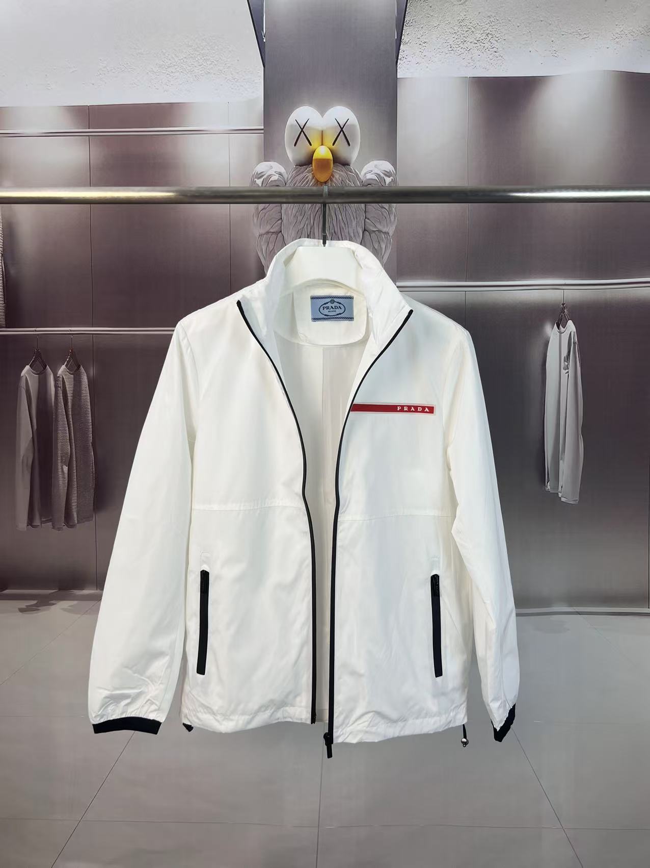 P190✨✨
 Prada 普拉达 2025秋冬新款 立领风衣夹克外套 薄款冲锋衣 经典红胶条logo 官网同步   原版定做五金拉链 走线工整 上身效果完美 男士休闲外套
颜色：白色
尺码：M-3XL