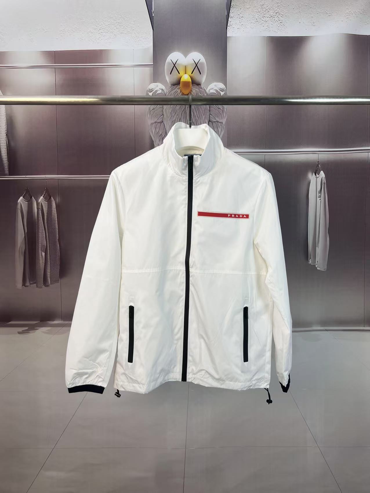 P190✨✨
 Prada 普拉达 2025秋冬新款 立领风衣夹克外套 薄款冲锋衣 经典红胶条logo 官网同步   原版定做五金拉链 走线工整 上身效果完美 男士休闲外套
颜色：白色
尺码：M-3XL