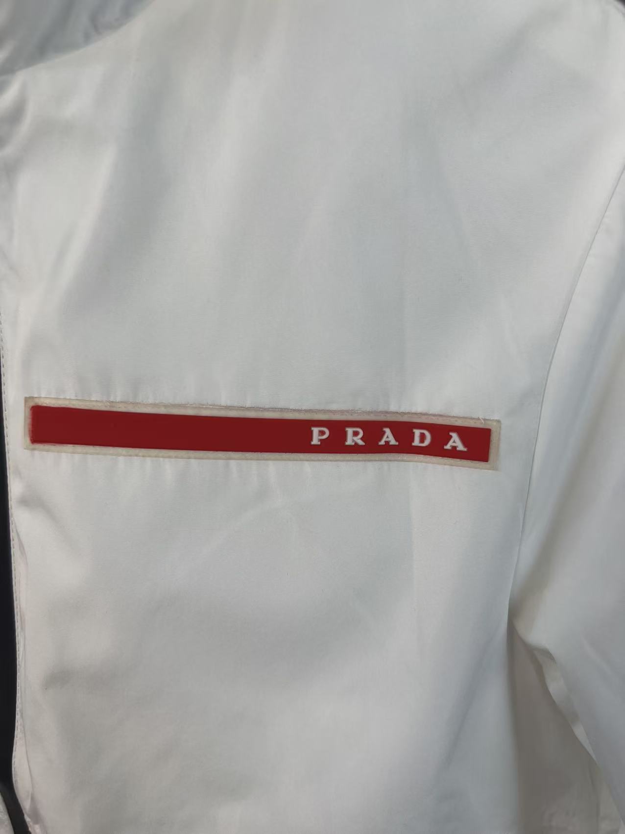 P190✨✨
 Prada 普拉达 2025秋冬新款 立领风衣夹克外套 薄款冲锋衣 经典红胶条logo 官网同步   原版定做五金拉链 走线工整 上身效果完美 男士休闲外套
颜色：白色
尺码：M-3XL