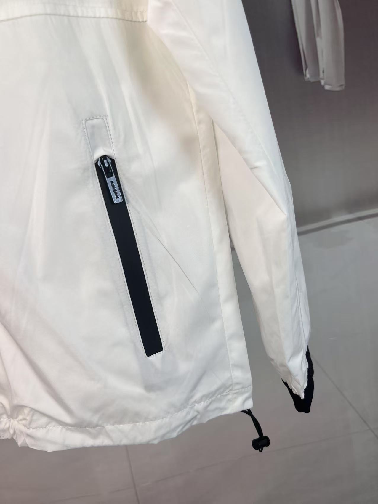 P190✨✨
 Prada 普拉达 2025秋冬新款 立领风衣夹克外套 薄款冲锋衣 经典红胶条logo 官网同步   原版定做五金拉链 走线工整 上身效果完美 男士休闲外套
颜色：白色
尺码：M-3XL