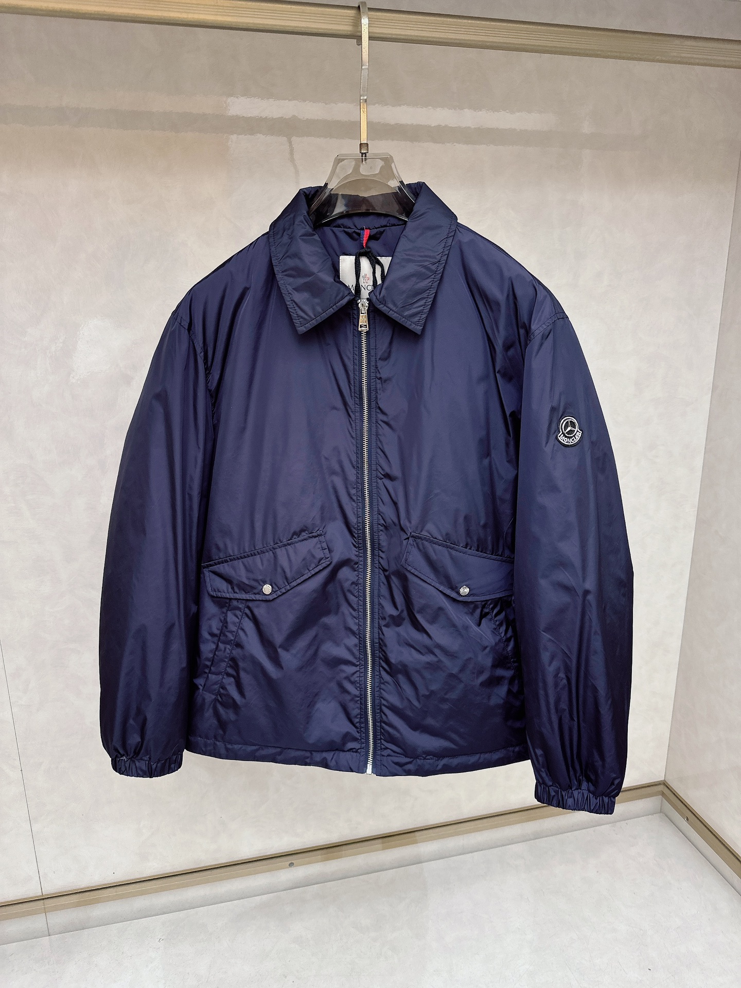 NO:647007,Mouthless MON X Mercedes-Benz jointly branded lightweight lapel jacket!  It adopts a classic lapel design, the overall shape is simple and elegant, and the lines are smooth. It is a versatile jacket style. The length reaches about the waist, making it suitable for daily wear and various casual occasions.  The fabric components are 83 polyamide (nylon) and 17 elastic fiber. The polyamide material makes the jacket wear-resistant, wrinkle-resistant and has certain windproof properties, while the elastic fiber increases the elasticity of the fabric, making it easier to wear. The lining is polyester fiber, which is smooth and comfortable and helps to improve the wearing experience. At the same time, the wash label indicates that it contains animal-based non-textile ingredients.  The overall color is dark blue, relatively low-key and calm. There is the iconic Monc brand logo patch on the left arm. In the middle of the logo is the Mercedes-Benz three-pointed star logo, and the word 'MON' is embroidered on the outer ring, highlighting the joint identity. There is a black and white printing area on the back, with car interior related patterns printed on it, and the word 'monc', which adds a sense of fashion and design.  The lapel design has neat lines, which can show a capable temperament when wearing. The zipper puller with the Mercedes-Benz three-pointed star logo on the top of the zipper at the collar. The zipper opening and closing design, with the Mercedes-Benz three-pointed star logo on the zipper puller, is exquisite and brand-recognizable, and the zipper is smooth and durable. There are two symmetrical flap pockets on the front, and the pocket flaps are equipped with snap buttons, which are convenient for storing small items and can play a certain role in fixing them.  , the snap buttons may also have related brand elements. The cuffs and hem are designed with elastic cuffs, which help to prevent wind and warmth while making the overall shape more neat!  Color Navy Size 48-56,,Moncler,jackets & coats,jackets & coats,alexander wang19860909蒙口 MON X 梅赛德斯奔驰联名轻薄翻领夹克外套！采用经典的翻领设计,整体版型简约大方,线条流畅 ,属于百搭的夹克款式.长度大概到腰部位置,适合日常穿着以及多种休闲场合. 面料成分是83聚酰胺（尼龙）和17弹性纤维,聚酰胺材质使得外套耐磨、抗皱且有一定的防风性能,弹性纤维则增加了面料的弹性,穿着活动更加自如.里料为聚酯纤维,顺滑舒适,有助于提升穿着体验.同时,水洗标提示包含动物性非纺织成分 . 整体为深蓝色,较为低调沉稳.左臂位置有标志性的Monc品牌徽标贴片,徽标中间是奔驰的三叉星标志,外圈刺绣有“MON”字样,彰显联名身份.背面拼接有一块黑白印花区域,印有汽车内饰相关图案,并且有“monc”字样,增加了时尚感与设计感. 翻领设计,线条利落,穿着时可以展现干练的气质.领口处拉链顶端带有奔驰三叉星标志的拉链头.拉链开合设计,拉链头上有奔驰的三叉星标志,精致且具有品牌辨识度,拉链顺滑耐用.正面设有两个对称的带盖口袋,口袋盖上配有按扣,方便存放小物件且能起到一定的固定作用 ,按扣上可能也带有相关品牌元素.袖口和下摆均采用弹性收口设计,有助于防风保暖,同时使整体造型更加利落！ 颜色藏青色 尺码48-56,,Moncler,jackets & coats,jackets & coats,alexander wang,Men's clothing