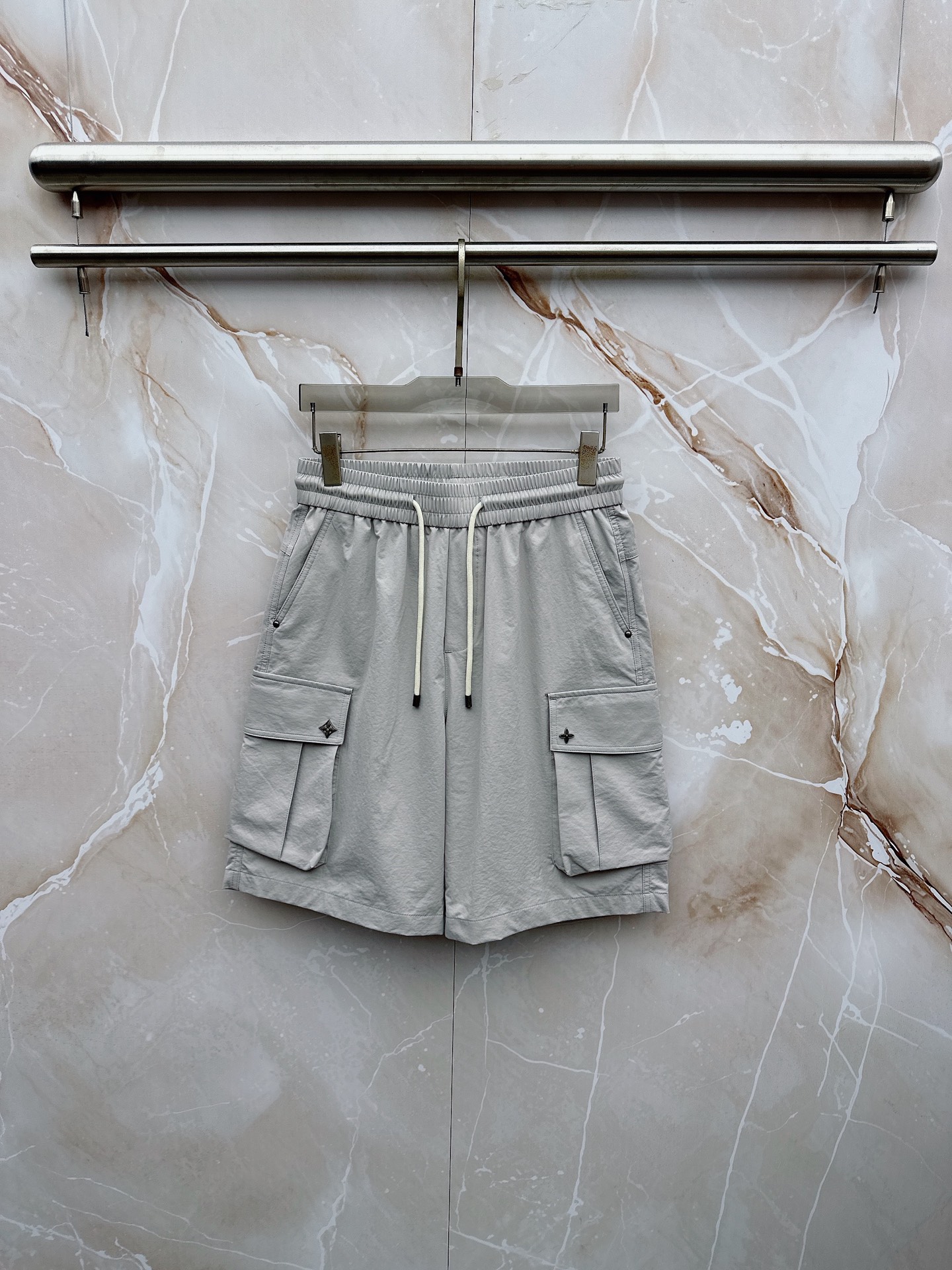 NO:907045,LV 2026 spring and summer new cargo shorts, continuing the classic Cargo  Pocket design, two-dimensional three-dimensional large pockets on both sides combine practicality and style. The drawstring elastic waistband adapts to various body shapes and easily creates a casual street posture. The fabric is made of light and breathable cotton blend material, which is soft and skin-friendly. It is refreshing and not stuffy to wear in spring and summer. The drapey fabric naturally modifies the leg shape and brings a lazy atmosphere when walking. The details are embellished with metal buttons and exquisite brand logos, highlighting quality in a low-key manner. The overall style combines the tough lines of Japanese workwear.  The stripes have a relaxed feel with American casual, with neat silhouettes for outdoor functions without losing the trendy attitude of urban streets. Whether it is daily commuting, weekend outings or sports and fitness, they can be easily controlled and show effortless fashion. In the spring and summer of 2026, let these cargo shorts become a versatile tool in your wardrobe. It uses simple colors and practical designs to interpret the new generation of street aesthetics, and easily wears the perfect balance of high-end and comfort. 29-38, louis  vuitton,shorts,19860909LV 2026春夏新品工装短裤,延续经典Cargo Pocket设计,双侧立体大口袋兼具实用性与造型感,抽绳松紧腰头适配各种身形,轻松打造随性街头姿态.面料选用轻薄透气的棉质混纺材质,触感柔软亲肤,春夏穿着清爽不闷热,垂坠感十足的面料自然修饰腿型,走动间自带慵懒氛围.细节处点缀金属纽扣与精致品牌标识,低调中彰显品质.整体风格融合日系工装的硬朗线条与美式休闲的松弛感,既有户外机能的利落轮廓,又不失都市街头的潮流态度.无论是日常通勤、周末出游还是运动健身,都能轻松驾驭,展现不费力的时髦感.2026春夏,让这条工装短裤成为你衣橱里的百搭利器,用简约色彩与实用设计诠释新一代街头美学,轻松穿出高级感与舒适度的完美平衡.29-38,,louis vuitton,shorts,,Men's clothing
