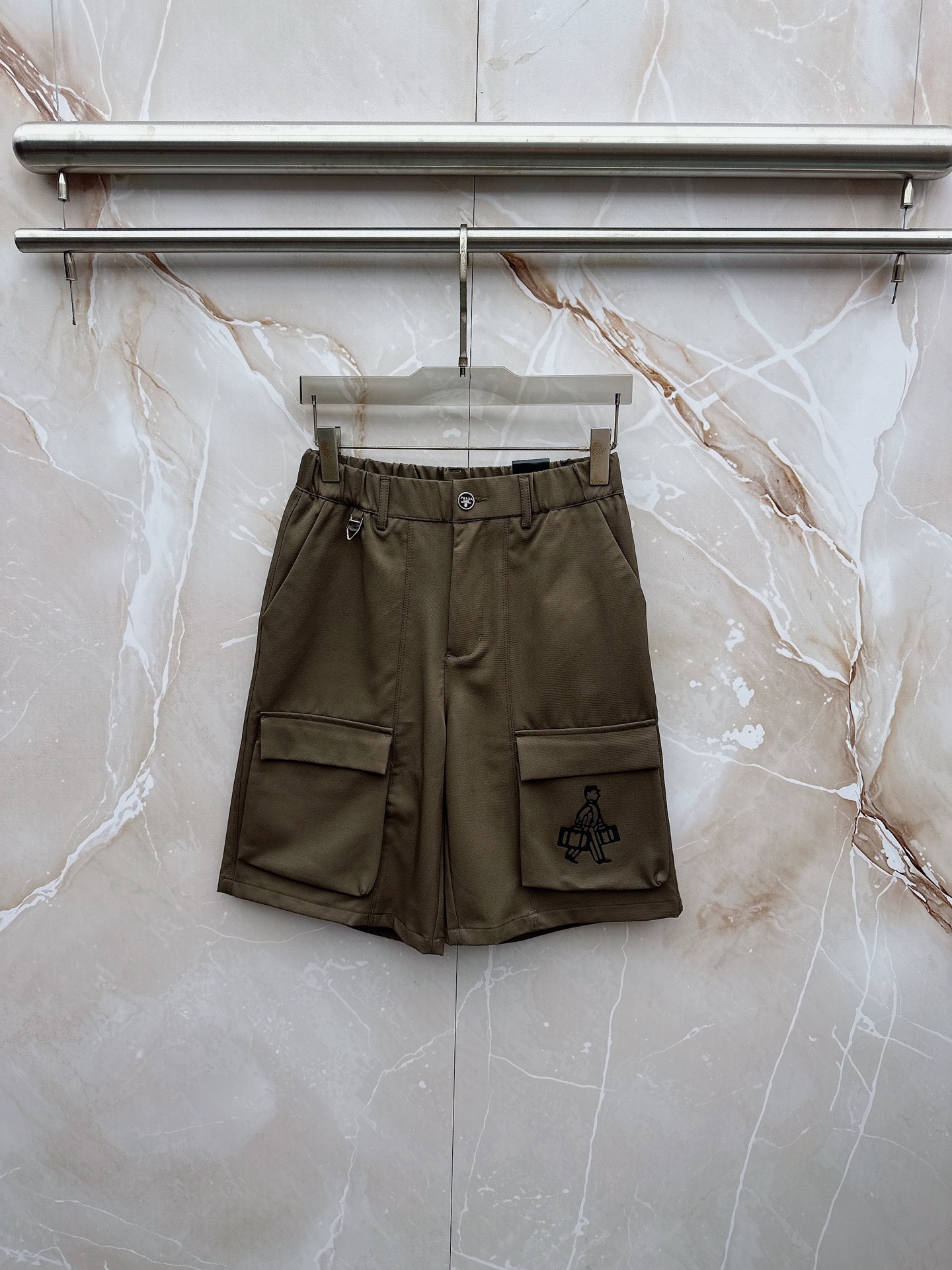 NO:907040,Prada 2026 spring and summer new cargo shorts continue the classic Cargo  Pocket design, two-dimensional three-dimensional large pockets on both sides combine practicality and style. The drawstring elastic waistband adapts to various body shapes and easily creates a casual street posture. The fabric is made of light and breathable cotton blend material, which is soft and skin-friendly, suitable for spring and summer.  It is refreshing and not stuffy to wear, and the drapey fabric naturally modifies the shape of the legs, giving it a lazy atmosphere when walking. The details are embellished with metal buttons and exquisite brand logos, highlighting quality in a low-key manner. The overall style combines the tough lines of Japanese workwear with American style  They have a casual and relaxed feel, with neat silhouettes for outdoor functions, but without losing the trendy attitude of urban streets. Whether it is daily commuting, weekend outings or sports and fitness, they can be easily controlled and show effortless fashion. In the spring and summer of 2026, make these cargo shorts a versatile tool in your wardrobe. It uses simple colors and practical designs to interpret the new generation of street aesthetics, and easily wears the perfect balance of high-end and comfort. M-3XL,, prada, shorts,19860909普拉达 2026春夏新品工装短裤,延续经典Cargo Pocket设计,双侧立体大口袋兼具实用性与造型感,抽绳松紧腰头适配各种身形,轻松打造随性街头姿态.面料选用轻薄透气的棉质混纺材质,触感柔软亲肤,春夏穿着清爽不闷热,垂坠感十足的面料自然修饰腿型,走动间自带慵懒氛围.细节处点缀金属纽扣与精致品牌标识,低调中彰显品质.整体风格融合日系工装的硬朗线条与美式休闲的松弛感,既有户外机能的利落轮廓,又不失都市街头的潮流态度.无论是日常通勤、周末出游还是运动健身,都能轻松驾驭,展现不费力的时髦感.2026春夏,让这条工装短裤成为你衣橱里的百搭利器,用简约色彩与实用设计诠释新一代街头美学,轻松穿出高级感与舒适度的完美平衡.M-3XL,,prada,shorts,,Men's clothing
