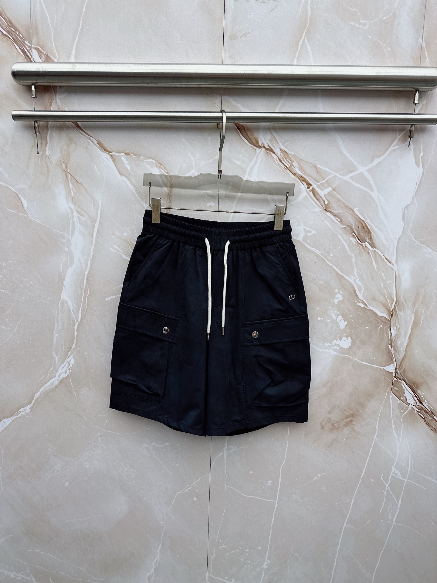 NO:932803,Dior's 2026 spring and summer new cargo shorts continue the classic Cargo  Pocket design, two-dimensional three-dimensional large pockets on both sides combine practicality and style. The drawstring elastic waistband adapts to various body shapes and easily creates a casual street posture. The fabric is made of light and breathable cotton blend material, which is soft and skin-friendly. It is refreshing and not stuffy to wear in spring and summer. The drapey fabric naturally modifies the leg shape and brings a lazy atmosphere when walking. The details are embellished with metal buttons and exquisite brand logos, highlighting quality in a low-key manner. The overall style combines the tough lines and beauty of Japanese workwear.  They have a casual and relaxed feel, with neat silhouettes for outdoor functions without losing the trendy attitude of urban streets. Whether it is daily commuting, weekend outings or sports and fitness, they can be easily controlled and show effortless fashion. In the spring and summer of 2026, make these cargo shorts a versatile tool in your wardrobe. It interprets the new generation of street aesthetics with simple colors and practical design, and can easily wear it to achieve the perfect balance of high-end and comfort. M-4XL,, dior, shorts,19860909迪奥 2026春夏新品工装短裤,延续经典Cargo Pocket设计,双侧立体大口袋兼具实用性与造型感,抽绳松紧腰头适配各种身形,轻松打造随性街头姿态.面料选用轻薄透气的棉质混纺材质,触感柔软亲肤,春夏穿着清爽不闷热,垂坠感十足的面料自然修饰腿型,走动间自带慵懒氛围.细节处点缀金属纽扣与精致品牌标识,低调中彰显品质.整体风格融合日系工装的硬朗线条与美式休闲的松弛感,既有户外机能的利落轮廓,又不失都市街头的潮流态度.无论是日常通勤、周末出游还是运动健身,都能轻松驾驭,展现不费力的时髦感.2026春夏,让这条工装短裤成为你衣橱里的百搭利器,用简约色彩与实用设计诠释新一代街头美学,轻松穿出高级感与舒适度的完美平衡.M-4XL,,dior,shorts,,Men's clothing