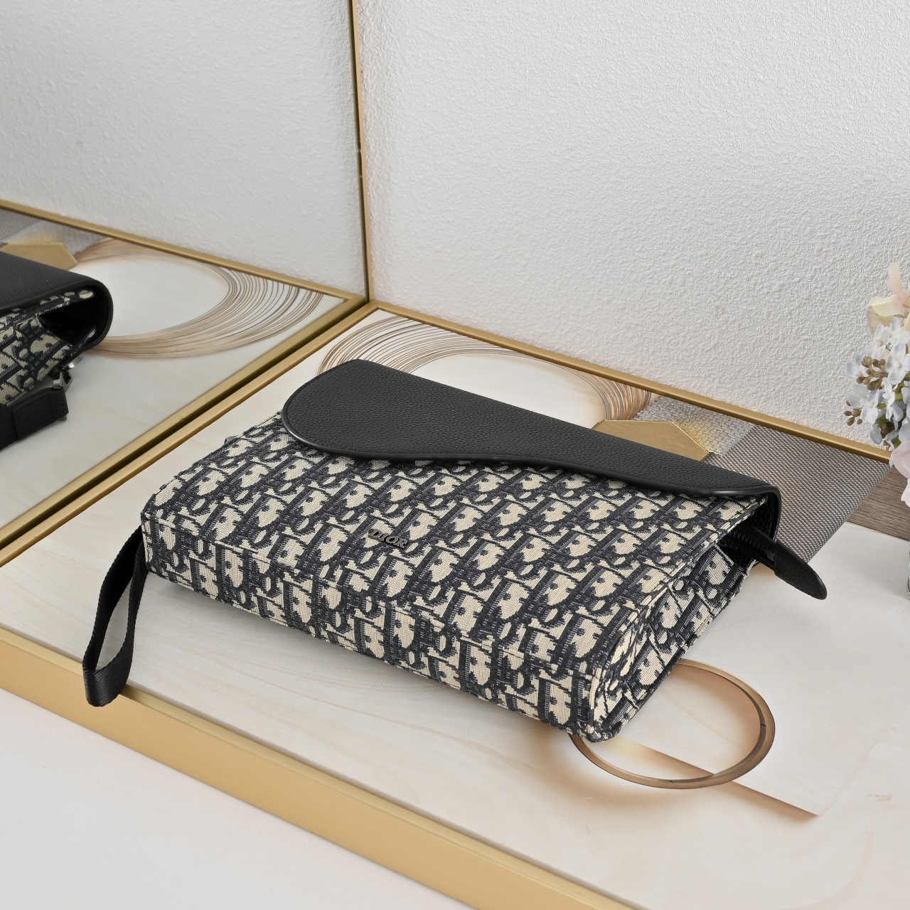 这款 A5 三角手拿包是  的全新主打单品。采用米色和黑色 Oblique 印花面料等材质精心制作，搭配黑色粒面牛皮革马
