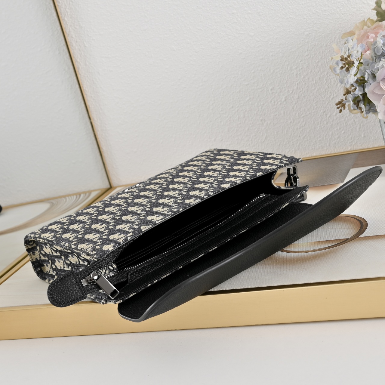 这款 A5 三角手拿包是  的全新主打单品。采用米色和黑色 Oblique 印花面料等材质精心制作，搭配黑色粒面牛皮革马
