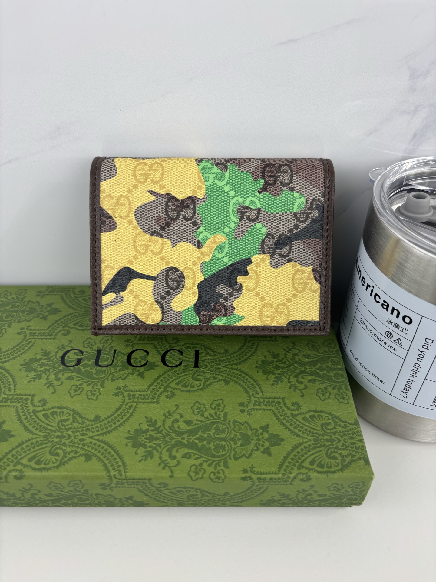 GUCCl生动迷彩结合别致配色，焕新演绎经典GG图案。这款短款卡包以大理石纹GG字母图案涂层织物打造，匠心融蕴双G细节。