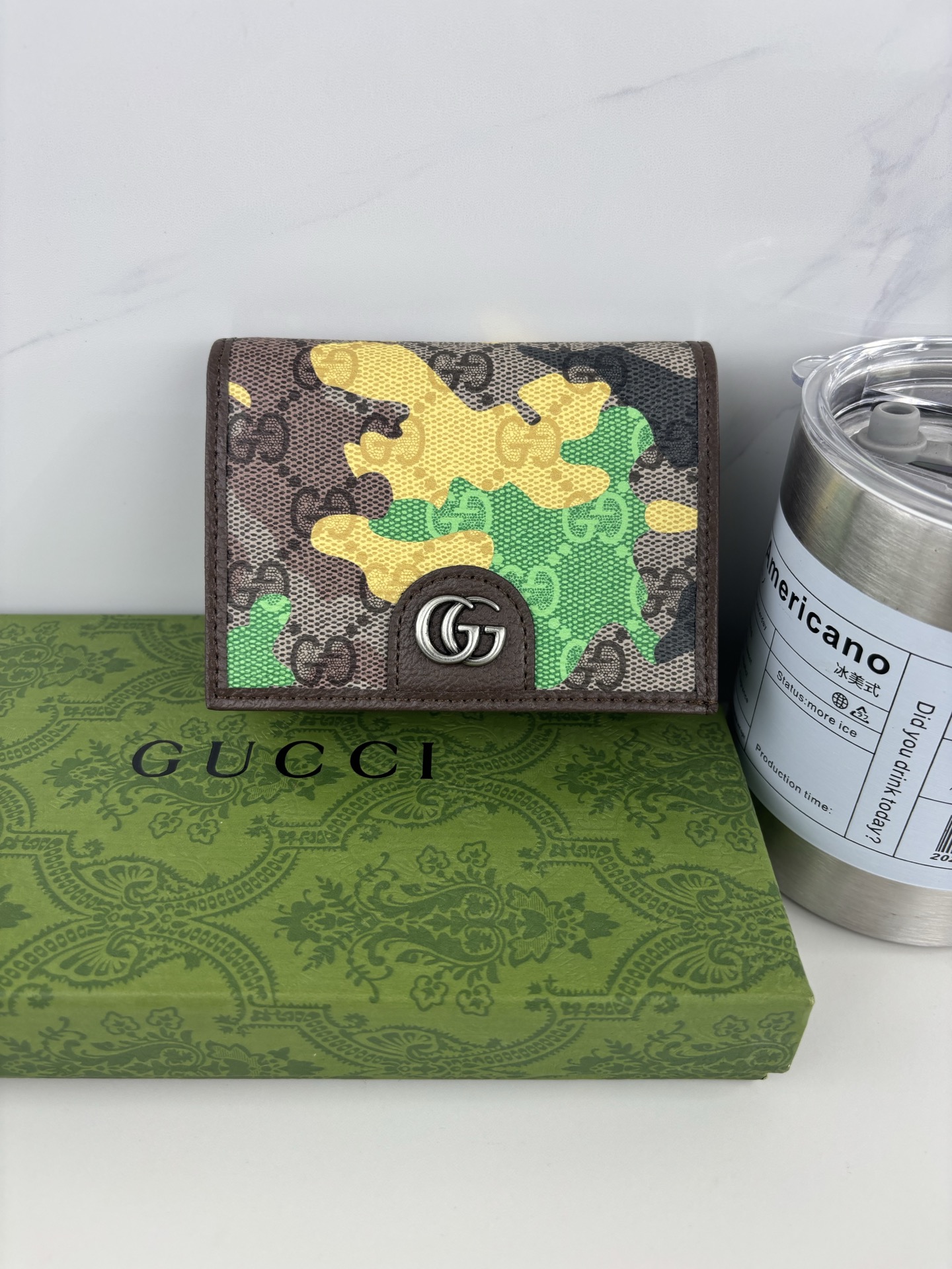 GUCCl生动迷彩结合别致配色，焕新演绎经典GG图案。这款短款卡包以大理石纹GG字母图案涂层织物打造，匠心融蕴双G细节。