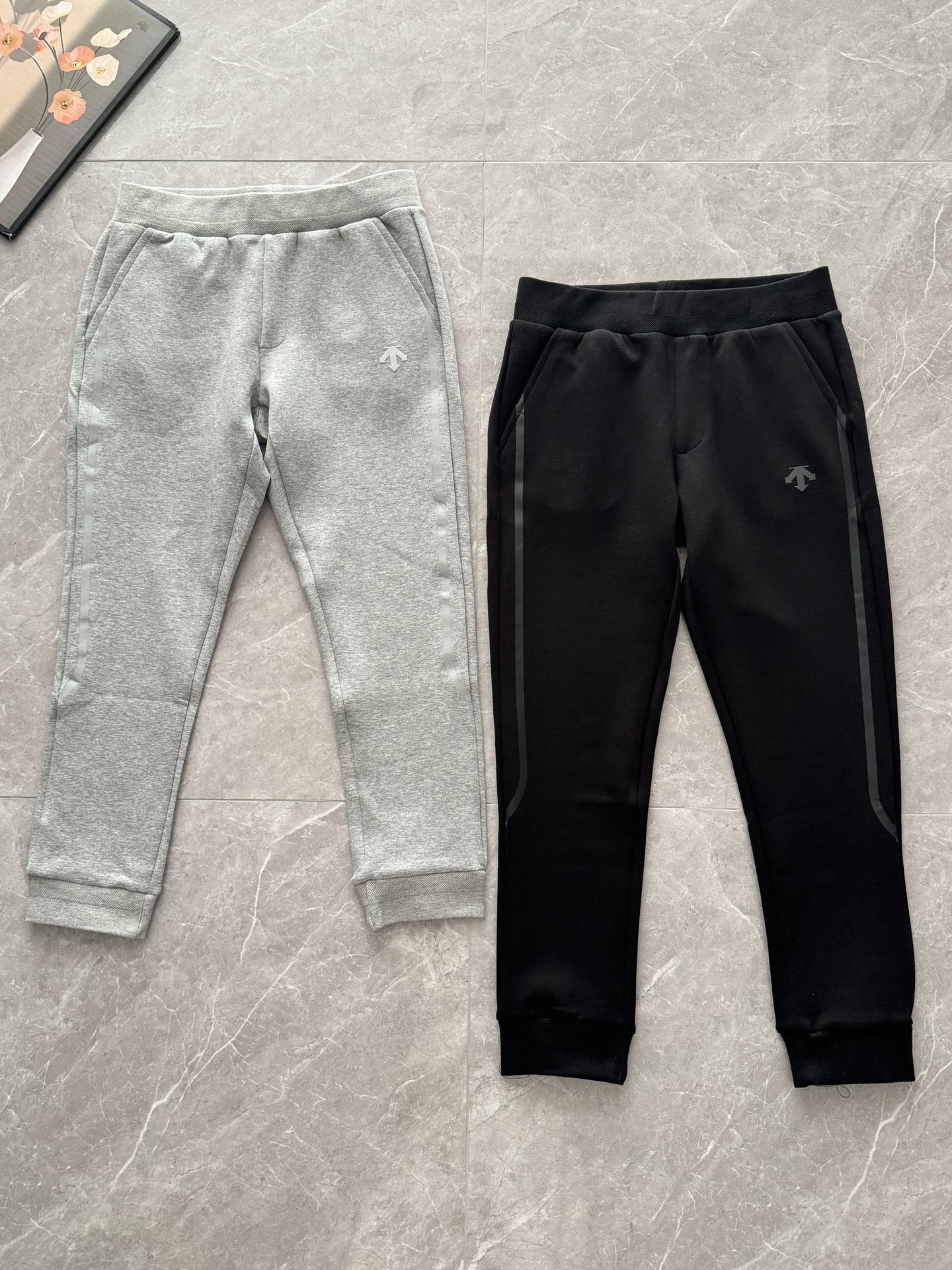 DESCENTE迪桑特原单男士弹力棉质束脚慢跑卫裤 型男魅力指数Max 摇身一变清爽大男孩Des 属于精致型男的穿搭“调剂品”原面料的含金量随便去对比 手感类似于空气棉/罗马布,拿在手中很有质感!不是传统纯棉毛圈的那种,闲暇之余的日常穿着,你需要这样一款版型到位、品质合格的休闲卫裤~卫裤这种单品不需要花哨设计,简单着来管它什么时尚圈的边边框框,我自成风格~ 立体束脚时尚实穿的版型,超舒适,裤腿渐收,贴合两侧压胶条设计,搭配便利的抽绳系带裤腰,轻松适配不同体型,上身利落不拖沓 裤型超赞,是日常通勤休闲都可以的那一款! 腰部加宽松紧腰更加贴合腰身+ 脚口松紧束口,腰口外置加粗的抽绳,上身利索 两侧口袋,以及后臀双口袋走线缝合的很整齐!裁剪的边缘大小也很齐 腰部加宽松紧腰更加贴合腰身,腰口外置加粗的顺色抽绳,上身利索,两侧口袋轻松储物,上身利落不拖沓,裤型超赞~ 口袋以及裤缝线流畅不卡顿,内侧的腰头下方和前后裆线连贯包边,又起到支撑性,穿一整天都不卡不磨不尴尬!➡️ 76%棉+17%聚酯纤维+7%氨纶的弹力棉质面料,采用最好的全棉精梳紧密赛络纺40支纱线,加75D的DTY聚酯纤维链接丝 ️ 两面加入满路的氨纶弹力丝,再经由纬编针织双面大圆机精密编织而成,打下坚实的胚布基础. 面料厚度刚刚好,高支高密的结构既透气又柔软,吸湿排汗,柔韧挺括有质感!上身更加亲肤 主要的是内里平整度更高 更细腻丝滑了~ 收到上手摸一下就知道了 区别市场通货! ⚠️有主标、洗标和吊牌 ️ 颜色 黑色 灰色 DES男士针织ESS横杠空气棉卫裤 腰围 裤长 臀围 推荐体重 M 76 94 100 110-130斤 L 80 96 104 130-150斤 XL 84 98 108 150-170斤 2XL 88 100 112 170-190斤 3XL 92 102 116 190-210斤 [手工测量存在2-3厘米的误差属正常现象, 建议尺码仅供参考]