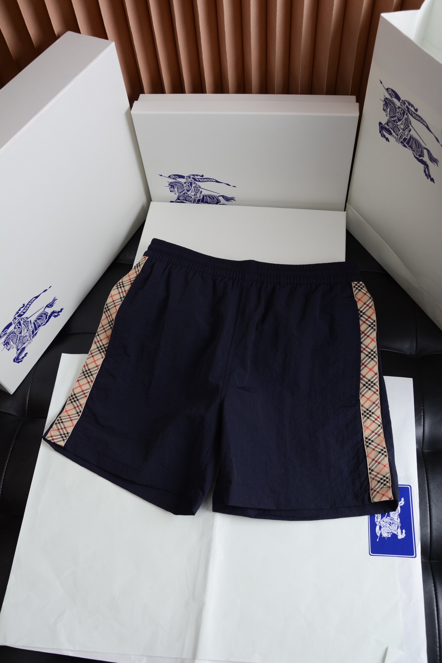 NO:786895,Navy blue hardware details have a warm texture and conceal brand recognition. The waistband adopts custom-made matte texture drawstring hardware. The surface has been treated with anti-oxidation plating. The color is fine and not dazzling. It harmoniously echoes the color of the trousers and is low-key and not exaggerated. The drawstring adjustment is smooth and not stuck, and there is no cheap loose feeling. The side pocket zipper uses brand-specific hardware, with precise bite and no noise when pulling. The details hide the exclusive luxury brand texture, which is restrained and high-end.  Fabric technology, light texture, breathable and quick-drying  The whole piece is made of brand-customized high-density polyester fiber woven fabric, which presents a delicate and natural texture on a solid color base. The side straps are woven into Burberry's iconic Vintage plaid, with neat alignment and bright colors.  The transition is soft, showing the British style under the light and shadow. The fabric is light and skin-friendly, with inherent stiffness. The upper body is not soft or clinging to the flesh. It has both breathability and drape. It is not stuffy and sweaty when worn in summer. It is not easy to deform or pill after being washed for a long time, and the texture is online.  The cut is neat and loose, not flattering on the body shape  Adopting a classic slightly loose straight fit, the trousers are neat and not draggy. The waistband is designed with elasticity, which can adapt to a wider range of waistlines without being too picky about the figure. The trousers are at a prime position above the knee, and the side plaid ribbon extends from the waistband to the trousers, visually modifying the proportions of the legs. The overall cut is clean and neat, and the upper body can modify the body shape without appearing restrictive. Whether it is paired with a T-shirt, a sweatshirt or a shirt, it can create a relaxed and high-end atmosphere.  These side plaid casual shorts are an excellent choice to bring Burberry's classics into daily life. They are low-key and unobtrusive, but full of texture details. They can easily be used as versatile textures in men's wardrobes. Burberry - Clothing, burberry, hoodie, sweatshirts, shorts, shirts, tees, t-shirt, gold,19860909海军蓝 五金细节温润质感,暗藏品牌辨识度 腰头采用定制的哑光质感抽绳五金头,表面经过防氧化电镀处理,色泽细腻不刺眼,与裤身色调和谐呼应,低调不浮夸.抽绳调节顺滑不卡顿,无廉价松动感.侧袋拉链采用品牌专用五金件,咬合精密,拉动时无杂音,细节里藏着专属的奢牌质感,内敛又高级. 面料工艺轻薄肌理,透气速干 整件采用品牌定制的高密聚酯纤维梭织面料,在纯色基底上呈现细腻自然的肌理感,侧边饰带织入Burberry标志性Vintage格纹,格纹对位工整,色彩过渡柔和,在光影下尽显英伦格调.面料触感轻薄亲肤,自带挺括度,上身不软塌、不贴肉,兼具透气性与垂坠感,夏天穿也不闷汗,久洗不易变形、起球,质感在线. 版型剪裁利落松弛,不挑身形 采用经典的微宽松直筒版型,裤型利落不拖沓,腰头为弹力松紧设计,对腰围的适配范围更广,不挑身材；裤长及膝上黄金位置,侧边格纹饰带从腰头延伸至裤脚,视觉上修饰腿型比例.整体剪裁干净利落,上身既能修饰身形,又不会显得拘谨,无论是搭配T恤、卫衣还是衬衫,都能穿出松弛又高级的氛围感. 这件侧边格纹休闲短裤,是把Burberry的经典穿进日常的绝佳选择,低调不张扬,却处处都是质感细节,轻松拿捏男士衣橱里的百搭质感担当.,博柏利-服装,burberry,hoodie,sweatshirts,shorts,shirts,tees，t-shirt,gold,,Women's clothing