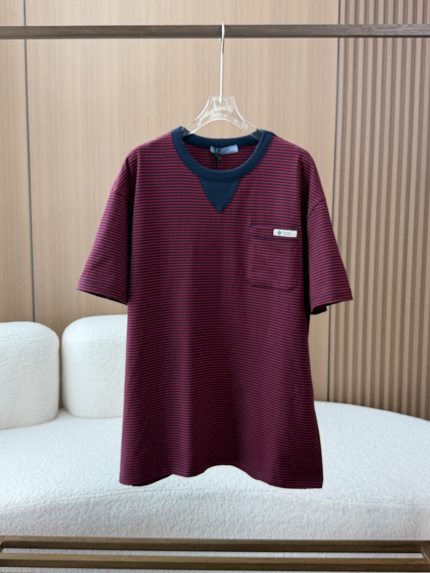 NO:874999,Prada/Prada Women's Oversize Style Striped Jersey T-Shirt Short Sleeve This T-shirt adopts the iconic Oversize silhouette, with a loose and dropped shoulder cut to create a casual and lazy atmosphere, while retaining clean lines, suitable for a variety of body shapes and layering styles. The main body of the body is made of dark blue and red two-color horizontal striped jersey fabric, which is soft and skin-friendly, has good drape and breathability, and is neatly routed, demonstrating the brand's strict control of quality.  The neckline adopts a double-layered contrasting color design. The outer layer is a ribbed round collar of the same color as the body, and the inner layer is superimposed with a brown V-shaped splicing patch, breaking the monotony of the conventional collar, forming a layered visual focus, and improving the modification effect of the neck line. There is a square patch pocket on the left chest, and a small white metal brand label is sewn at the pocket with the Prada logo clearly imprinted. It is both a practical decorative detail and a low-key conveyer of brand recognition.  The short-sleeved cuffs are designed with the same stripes as the body, and the edges are smooth and neat, echoing the loose silhouette of the body, and the overall style is unified and coordinated.  This T-shirt cleverly combines classic striped elements with modern silhouette design. It not only retains Prada's consistent high-end texture, but also uses details such as contrasting collars and iconic labels to create an outfit with both retro charm and contemporary fashion. It is suitable as a core item for daily looks or as the finishing touch in layering, prada, prada, versace, T-shirt, tees, t-shirt,19860909Prada/普拉达女士Oversize造型条纹平纹针织T恤短袖 这款T恤采用标志性的Oversize廓形,以宽松落肩剪裁打造随性慵懒的穿搭氛围,同时保留利落的线条感,适配多种身形与叠穿风格. 衣身主体采用深蓝红双色横条纹平纹针织面料,触感柔软亲肤,兼具良好的垂坠感与透气性,走线工整,彰显品牌对品质的严苛把控 领口处采用双层撞色设计,外层为与衣身同色的罗纹圆领,内层叠加一块棕色V形拼接饰片,打破常规领型的单调感,形成富有层次的视觉焦点,同时提升了颈部线条的修饰效果. 左胸位置设有一个方形贴袋,袋口处缝制一枚小巧的白色金属质感品牌标签,清晰印刻Prada标识,既作为实用的装饰细节,又低调传递品牌辨识度. 短袖袖口采用与衣身一致的条纹设计,边缘平整利落,与宽松的衣身廓形形成呼应,整体风格统一协调. 这款T恤将经典条纹元素与现代廓形设计巧妙融合,既保留了Prada一贯的高级质感,又通过撞色领部与标志性标签等细节,塑造出兼具复古韵味与当代时尚感的穿搭单品,适合作为日常造型的核心单品或叠穿层次中的点睛之笔,,prada,prada,versace,T-shirt,tees，t-shirt,,Women's clothing