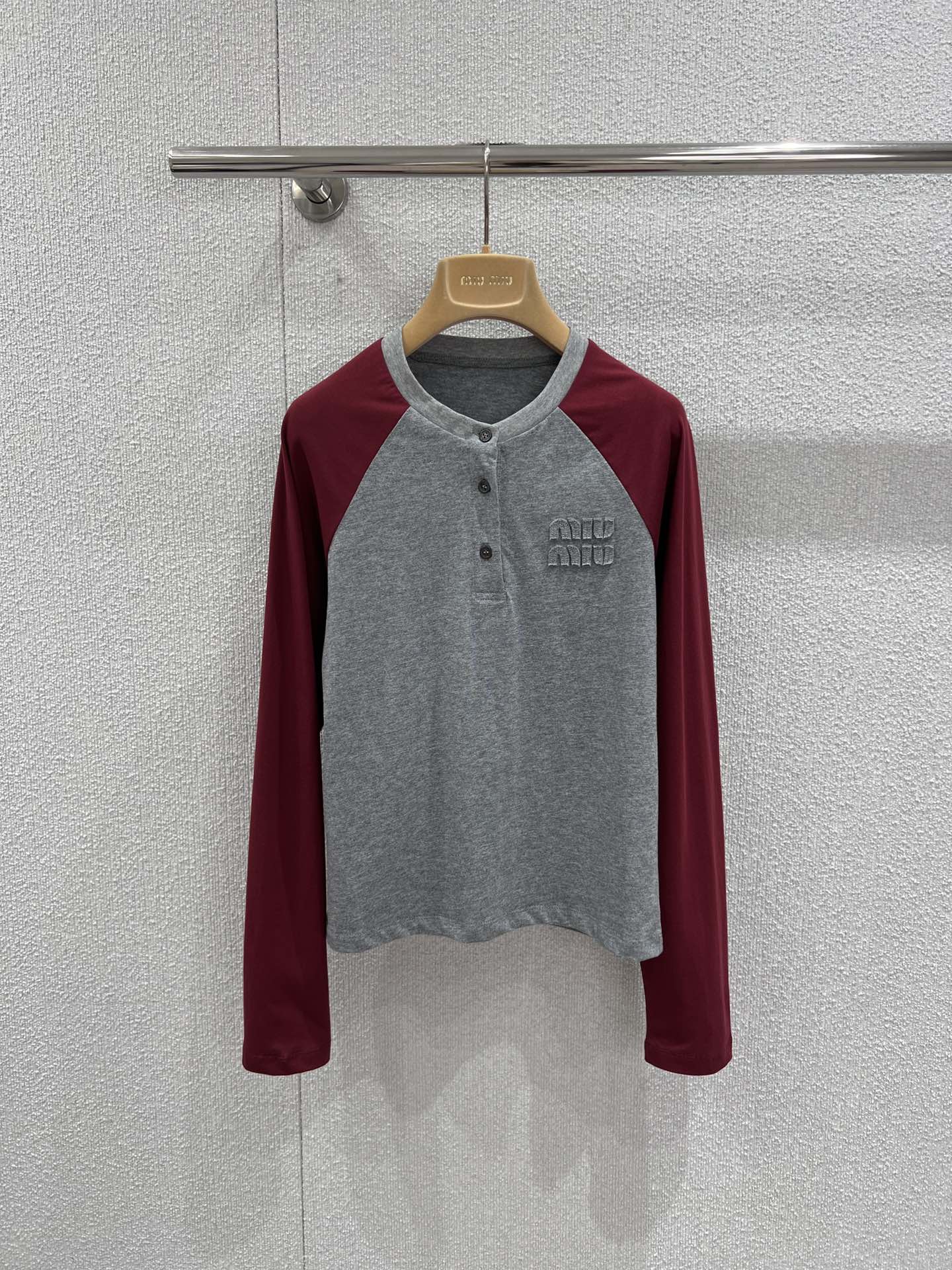 NO:717454,Support exchange Miu M*u 26Ss early spring new style gray and red patch-sleeved long-sleeved collar button T-shirt丨Exclusive high-end version!  Inspired by American retro baseball shirts, the classic raglan sleeve design is used to reshape the college style. The calm gray tones and warm red tones collide to create a vivid visual tension. The three-button detail on the neckline adds a sense of style. It can be opened to create a V-neck effect or buttoned to keep it neat. The three-dimensional appliqué logo on the chest is low-key for recognition, and the soft cotton blended fabric is comfortable.  It has a crisp feel and a well-fitting cut that fits the body shape but is not tight. Paired with a white work skirt, it is a sweet and cool girl style, and paired with jeans, it can be worn casually and relaxedly. It is a versatile item that can be worn layered or worn alone in early spring. Ready-made S/M/L real shot details, miumiu, skirts, jeans, tees, t-shirt,19860909支持换款 Miu M*u 26Ss早春新款 灰红拼袖长袖领扣T恤丨独家高版出品！以美式复古棒球衫为灵感,用经典插肩袖设计重塑学院风.沉稳灰调与热烈红调碰撞出鲜活的视觉张力,领口三颗纽扣细节增添了造型感,可敞开打造V领效果,也可扣合保持利落.胸前立体贴布绣Logo低调彰显辨识度,柔软的棉混纺面料兼具舒适度与挺括感,合身剪裁贴合身形却不紧绷.搭配白色工装裙是甜酷少女风,配牛仔裤又能穿出随性松弛感,是早春叠穿与单穿都出彩的百搭单品.现货发售S/M/L实拍细节图,,miumiu,skirts,jeans,tees，t-shirt,,Women's clothing