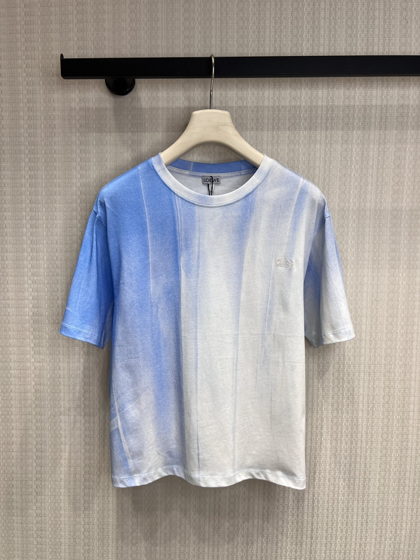 NO:839032,26 spring and summer new product Loe ** uses blue and white blooming as a pen to outline the gradient texture of the sky and waves on pure cotton fabric, bringing a cool and relaxing summer atmosphere. The dropped shoulder silhouette weakens the toughness of the lines, and the three-dimensional embroidered logo on the chest low-key injects brand texture. The short length is just suitable for high-waisted bottoms. It is a high-end item with a sense of breath for daily wear. Ready for sale smL,, loewe,1986090926春夏新品 Loe ** 以蓝白晕染为笔,在纯棉面料上勾勒出天空与海浪的渐变肌理,自带清冷松弛的夏日氛围.落肩廓形弱化了线条的硬朗,胸前的立体刺绣徽标低调注入品牌质感,短款衣长刚好适配高腰下装,是日常穿搭里自带呼吸感的高级单品.现货出售smL,,loewe,,Women's clothing