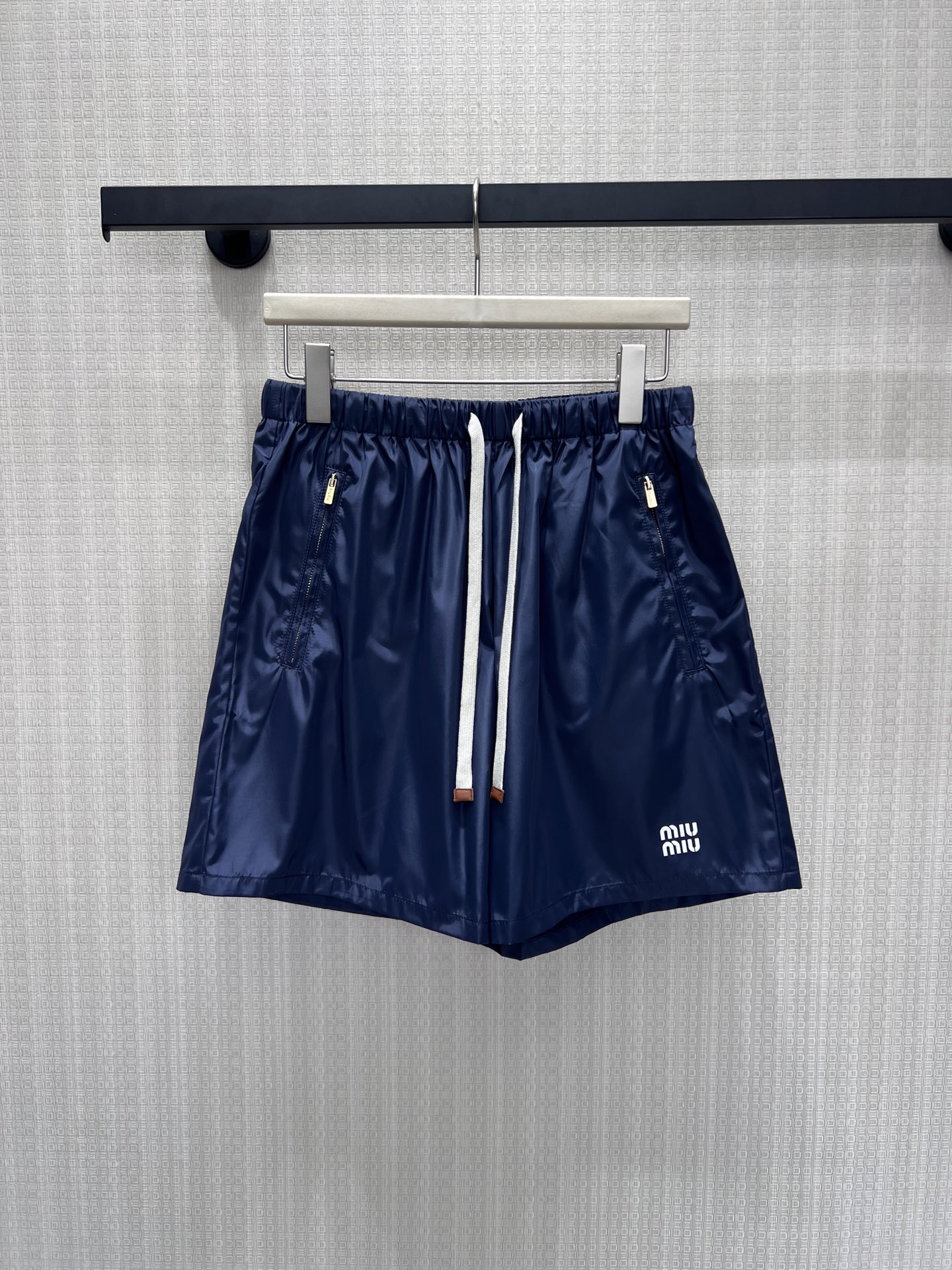 NO:865331,26 spring and summer new products  Miu** navy blue nylon shorts are the must-have for sweet and cool girls in summer. The neat navy blue background is matched with off-white drawstrings, and the contrasting design brings a refreshing texture. The side zipper pockets are both practical and neat. The trouser legs have exquisite brand embroidery, which is low-key and recognizable. The loose fit hides the flesh and makes you look slimmer. The nylon fabric is light and wrinkle-proof. You can easily achieve a relaxed and elegant college feel when worn alone or with stockings. Available now smL,, miumiu, shorts,1986090926春夏新品 Miu**藏青尼龙短裤,是甜酷少女的夏日刚需.利落藏青底色搭配米白抽绳,撞色设计自带清爽质感,侧拉链口袋兼顾实用与利落.裤脚精致品牌刺绣,低调又辨识度拉满,宽松版型藏肉显瘦,尼龙面料轻透防皱,单穿或搭配长袜都能轻松拿捏松弛又贵气的学院感.现货出售smL,,miumiu,shorts,,Women's clothing
