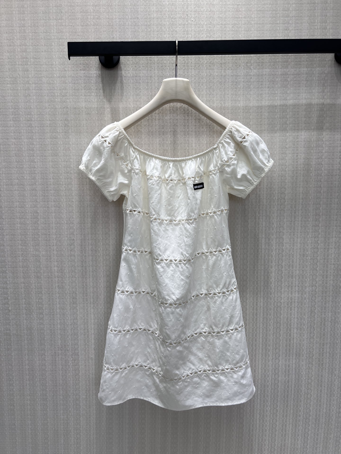 NO:893080,26 new spring and summer dress Miu* pure white hollow one shoulder  It fully presents the sweetness and elegance of Italian girls. The soft off-white cotton-feel fabric has its own texture, the one-line puff sleeves outline the soft shoulder and neck lines, and the layers of triangular hollow horizontal strips are arranged at random, which is transparent and light without losing the sense of layering. The small brand woven label on the chest is a low-key finishing touch, weakening the sweetness and adding to the sense of layering.  Adding a sense of light luxury. The straight short version is smart and reduces age, and the off-the-shoulder design fills the gentle atmosphere. It is suitable for vacations and afternoon tea dates. It is a gold-style little white dress with a pure and soft light. In stock 36/38/40,,miumiu,skirts,1986090926春夏新品 连衣裙 Miu*纯白镂空一字肩 把意式少女的清甜雅致尽数呈现.柔和米白棉感面料自带肌理,一字领泡泡袖勾勒柔美的肩颈线条,层层三角镂空横条错落排布,通透轻盈不失层次感.胸口小巧品牌织标低调点睛,弱化甜腻,增添轻奢辨识度.直筒短款版型灵动减龄,露肩设计温柔氛围感拉满,度假出游、下午茶约会都适配,是自带纯净柔光感的千金风小白裙.现货36/38/40,,miumiu,skirts,,Women's clothing