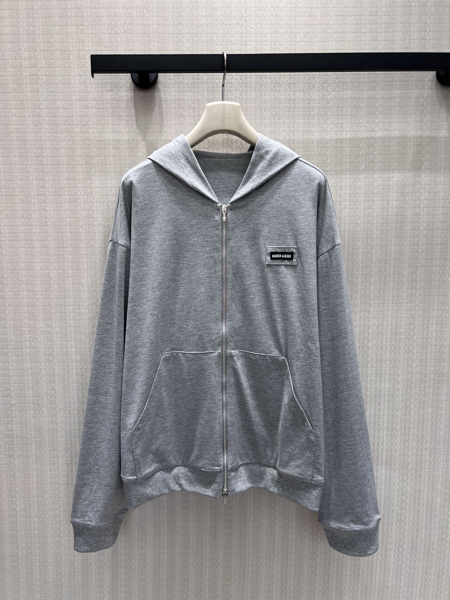 NO:893083,26 spring and summer new products  Miu** hemp gray hooded zipper sweatshirt interprets low-key casual aesthetics. The soft floral gray fabric is soft and smooth, delicate and skin-friendly with a matte high-end texture. Full zipper closure with classic kangaroo pocket, dropped shoulders and wide sleeves cut to relax and accommodate the body shape, not deliberately modified but with a lazy atmosphere. The mini woven label on the left chest is engraved with the brand logo in a low-key manner.  Abandon the exaggerated design and use minimalist lines to outline the Italian girly style. Wear it casually and refreshingly. It can be worn with a shirt inside or a coat outside. It is easy to wear in daily wear without revealing the exquisite elegance. In stock smL,, miumiu, hoodie, sweatshirts, shirts, hats,1986090926春夏新品 Miu**麻灰连帽拉链卫衣,诠释低调千金休闲美学.柔和花灰面料软糯垂顺,细腻亲肤自带哑光高级质感.全拉链开合搭配经典袋鼠兜,落肩阔袖剪裁松弛包容身形,不刻意修饰却自带慵懒氛围.左胸迷你织标低调镌刻品牌标识,摒弃浮夸设计,用极简线条勾勒意式少女格调.单穿随性清爽,内搭衬衫、外搭大衣皆适配,日常穿搭轻松拿捏不露声色的精致贵气.现货smL,,miumiu,hoodie,sweatshirts,shirts,hats,,Women's clothing