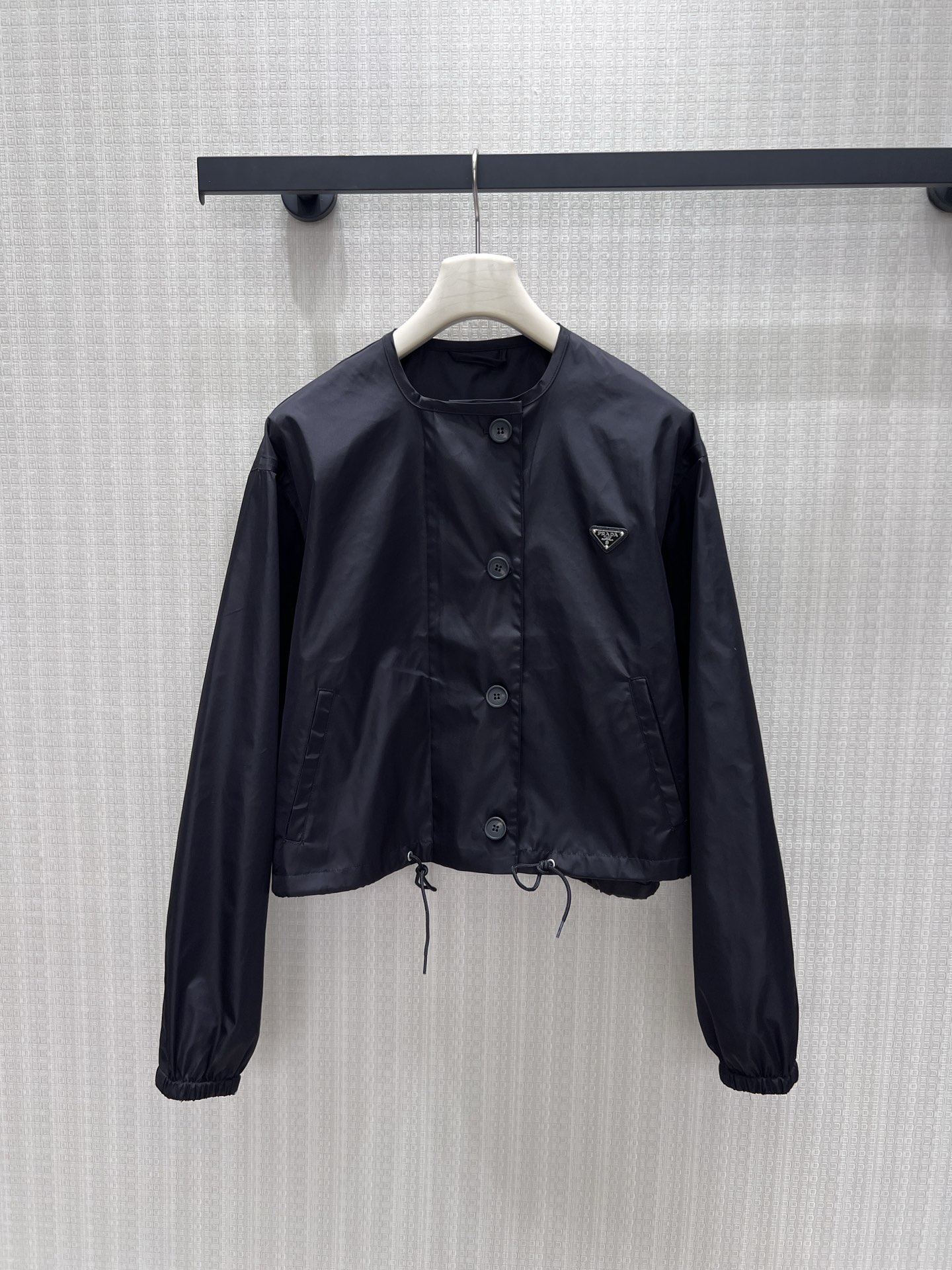 NO:954880,26 early autumn new Pra** black short round neck jacket, minimalist and neat Italian aesthetics. The iconic triangle logo is low-key embellishment on the body, and the single-row buttons are simple and elegant. The drawstring at the hem can be adjusted to the shape, and the cuffed sleeves are smart and relaxed. The crisp windproof fabric is of high quality, and the short cut optimizes body proportions. It is versatile and does not choose inner wear, taking into account both practical wear and style, making it easy to create a variety of advanced styles for commuting and leisure. Ready in stock smL  Actual detailed pictures,,prada,jackets & coats,jackets & coats,1986090926早秋新款 Pra**黑色短款圆领夹克外套,极简利落的意式美学.标志性三角徽标低调点缀衣身,单排纽扣简约大气.下摆抽绳可随心调节版型,收口袖型干练松弛.挺括防风面料质感上乘,短款剪裁优化身形比例.百搭不挑内搭,兼顾实穿与格调,轻松打造通勤、休闲多元高级造型.现货smL 实拍细节图,,prada,jackets & coats,jackets & coats,,Women's clothing