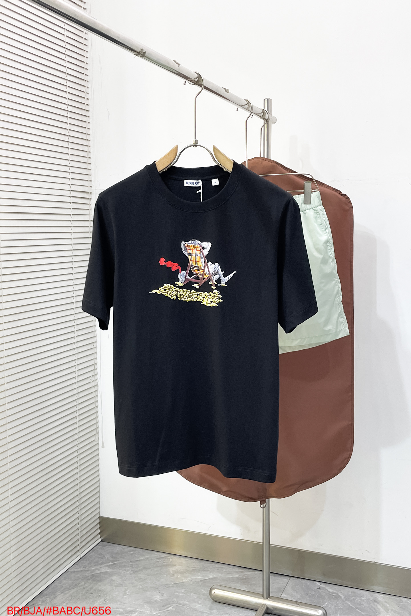 NO:841910,U656 BR Burberry 26ss  The new beach chair embroidered round neck short-sleeved T-shirt is made of 15-count heavyweight combed pure cotton plain fabric, weighing 230g. The fabric texture is tight and full, with strong structural support and skin-friendly breathability. It has been pre-shrunk and enzymatically pre-washed. It has excellent dimensional stability and can effectively resist the risks of deformation, wrinkling and yellowing caused by daily washing. Craftsmanship  It uses a dual process of digital printing + foaming, using high-precision digital direct injection technology to restore the level of detail of the beach lounger knight pattern and brand logo, and then uses environmentally friendly foaming glue for local three-dimensional embossing treatment, so that the pattern presents a rich relief texture and tactile levels. The ink color has strong adhesion, is washable and does not fall off, while retaining the soft and breathable properties of the fabric.  The version adopts a slightly loose and straight cut with dropped shoulders. The neckline is a double-needle ribbed round neck. It is combined with three-needle hemming technology to enhance the collar's stretch resistance and prevent it from loosening after long-term wear. The cuffs and hem are processed by flat-turn double-needle curling, with neat and neat lines. The size is S. M. L. XL. Complete, burberry, T-shirt, tees, t-shirt,19860909U656 BR 巴宝莉 26ss 新款海滩椅刺绣圆领短袖T恤,采用15支重磅精梳纯棉平纹面料织造,克重达230g,布面肌理紧密饱满,兼具强韧结构支撑力与亲肤透气性,经预缩定型与酵素预洗处理,尺寸稳定性优异,可有效抵御日常洗涤带来的变形、起皱与泛黄风险,工艺上采用数码印花+发泡双重工艺,通过高精度数码直喷技术还原沙滩躺椅骑士图案与品牌标识的细节层次,再以环保发泡胶浆进行局部立体起凸处理,使图案呈现出丰富的浮雕肌理与触感层次,墨色附着力强、耐洗不脱落,同时保留面料的柔软透气属性 版型上采用微宽松落肩直身剪裁,领口为双针罗纹圆领,配合三本针锁边工艺强化领型抗拉伸性,久穿不易松垮；袖口与下摆采用平车双针卷边处理,线条利落工整 码数S. M. L. XL三标齐全,,burberry,T-shirt,tees，t-shirt,,Men's clothing