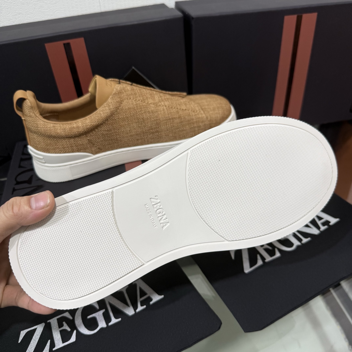 Zegna/杰尼亚 SECONDSKIN Triple Stitch&trade; 休闲运动鞋，帆布系列
这款低帮运动鞋的鞋面光滑柔软。饰以标志性三重交叉松紧细节，致敬品牌精裁夹克的手工缝制工艺。设计轻盈，与白色橡胶鞋底相得益彰，专为快节奏的生活方式打造。这款鞋汲取手套制作灵感，融汇世代工匠经验智慧，选用新西兰顶级小牛皮制作，成就轻盈质地，精致衬里结合非凡韧性。带来独一无二的贴合感。非常轻盈的橡胶外底上点缀双条纹 Logo 运动细节，以超轻结构重新诠释标志性鞋款。领口部位鹿皮面料反车做法，无内裡车中底套楦做法。易穿脱套脚交叉松紧带和 3D&ldquo;波纹&rdquo;设计。鞋舌热压品牌名称。
后跟加贴 TPU 双条纹品牌 Logo 饰条，鞋身空胶做法，周圈加车大底缝线。轻盈的高弹力橡胶外底背面和可拆卸脚床饰 Zegna 标识，为这款运动鞋增添现代动感气息。
皮鞋码数:39/40/41/42/43/44/45/46/47 
专柜包装，现货