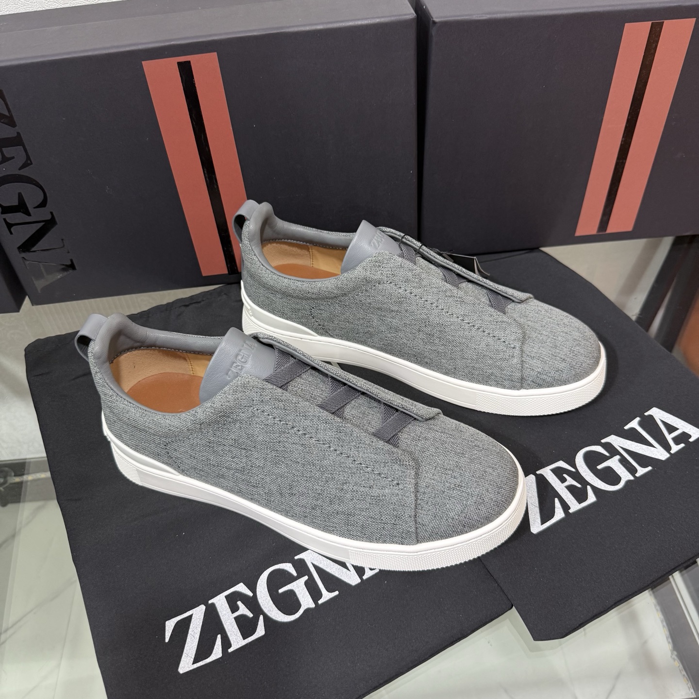 Zegna/杰尼亚 SECONDSKIN Triple Stitch&trade; 休闲运动鞋，帆布系列
这款低帮运动鞋的鞋面光滑柔软。饰以标志性三重交叉松紧细节，致敬品牌精裁夹克的手工缝制工艺。设计轻盈，与白色橡胶鞋底相得益彰，专为快节奏的生活方式打造。这款鞋汲取手套制作灵感，融汇世代工匠经验智慧，选用新西兰顶级小牛皮制作，成就轻盈质地，精致衬里结合非凡韧性。带来独一无二的贴合感。非常轻盈的橡胶外底上点缀双条纹 Logo 运动细节，以超轻结构重新诠释标志性鞋款。领口部位鹿皮面料反车做法，无内裡车中底套楦做法。易穿脱套脚交叉松紧带和 3D&ldquo;波纹&rdquo;设计。鞋舌热压品牌名称。
后跟加贴 TPU 双条纹品牌 Logo 饰条，鞋身空胶做法，周圈加车大底缝线。轻盈的高弹力橡胶外底背面和可拆卸脚床饰 Zegna 标识，为这款运动鞋增添现代动感气息。
皮鞋码数:39/40/41/42/43/44/45/46/47 
专柜包装，现货