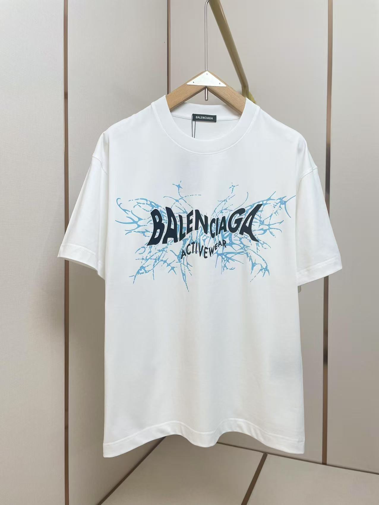 NO:428185,Balenciaga Activewear series short-sleeved T-shirts adopt the brand's iconic minimalist silhouette design. The front of the T-shirt is printed with 'BALENCIAGA ACTIVEWEAR' in black font, and the letter edges have blue crack ink dyeing special effects, injecting street art into the basic style. The contrasting color design of blue and black ink splashing font and black and white background continues the brand's main deconstructive aesthetic language in recent years. Shoulder shoulder pressure strips 280 grams pure cotton fabric is comfortable and breathable, black and white, same as men and women. S-XXL,,balenciaga,balenciaga,T-shirt,tees,t-shirt,alexander wang19860909巴黎世家 Activewear系列短袖T恤,采用品牌标志性的极简廓形设计.T恤正面以黑色字体印刷'BALENCIAGA ACTIVEWEAR'字样,字母边缘带有蓝色裂纹墨染特效,为基本款注入街头艺术感.蓝黑泼墨字体与黑色白色底色的撞色设计,延续了品牌近年主打的解构美学语言.肩部通肩压条 280克纯棉面料舒适透气 黑白双色 男女同款 码数S-XXL,,balenciaga,balenciaga,T-shirt,tees，t-shirt,alexander wang,Men's clothing