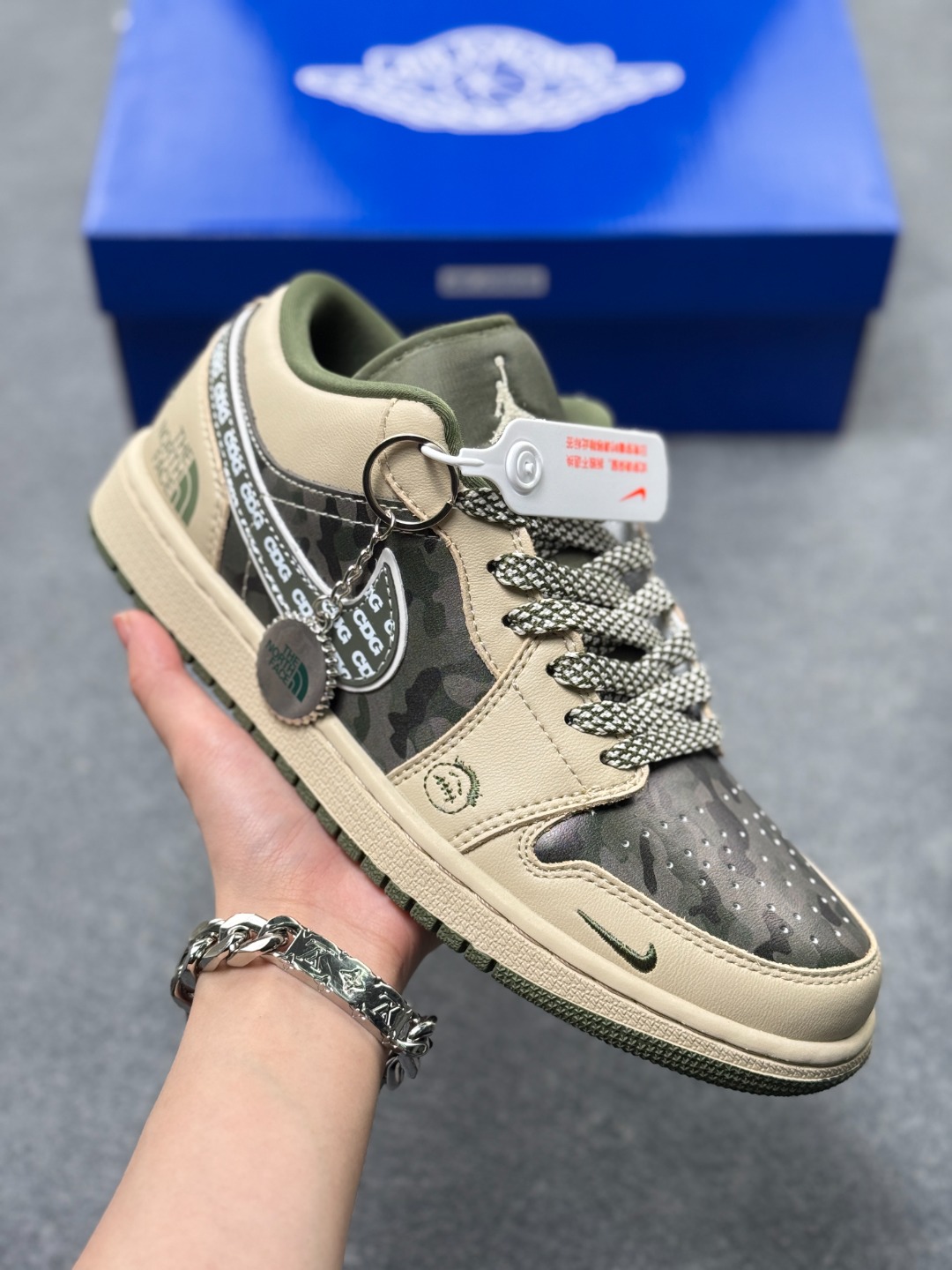 💰240
Air Jordan 1 Low x 北面 x CDG 联名款｜野性与潮流的碰撞。当飞人图腾邂逅户外传奇，再融合先锋时尚的基因，这双Air Jordan 1 Low QG1988-017直接把跨界联名的质感拉满！浅卡其色鞋身搭配墨绿迷彩拼接，皮革与耐磨材质的碰撞，既有AJ1经典的复古轮廓，又注入了The North Face的户外硬核气质。鞋侧Swoosh满印CDG标识，后跟北面logo醒目点缀，三重品牌元素的融合毫不违和，每一处细节都透着潮流与机能的双重魅力。粗织鞋带、撞色包边的设计，让这双鞋不仅是穿搭利器，更暗藏户外探索的野性；低帮版型兼顾日常上脚的舒适与百搭，不管是街头潮搭还是轻户外造型，都能轻松hold住。这双集AJ的经典、北面的硬核、CDG的先锋于一体的联名款，是潮流玩家和户外爱好者都无法拒绝的收藏级单品！
