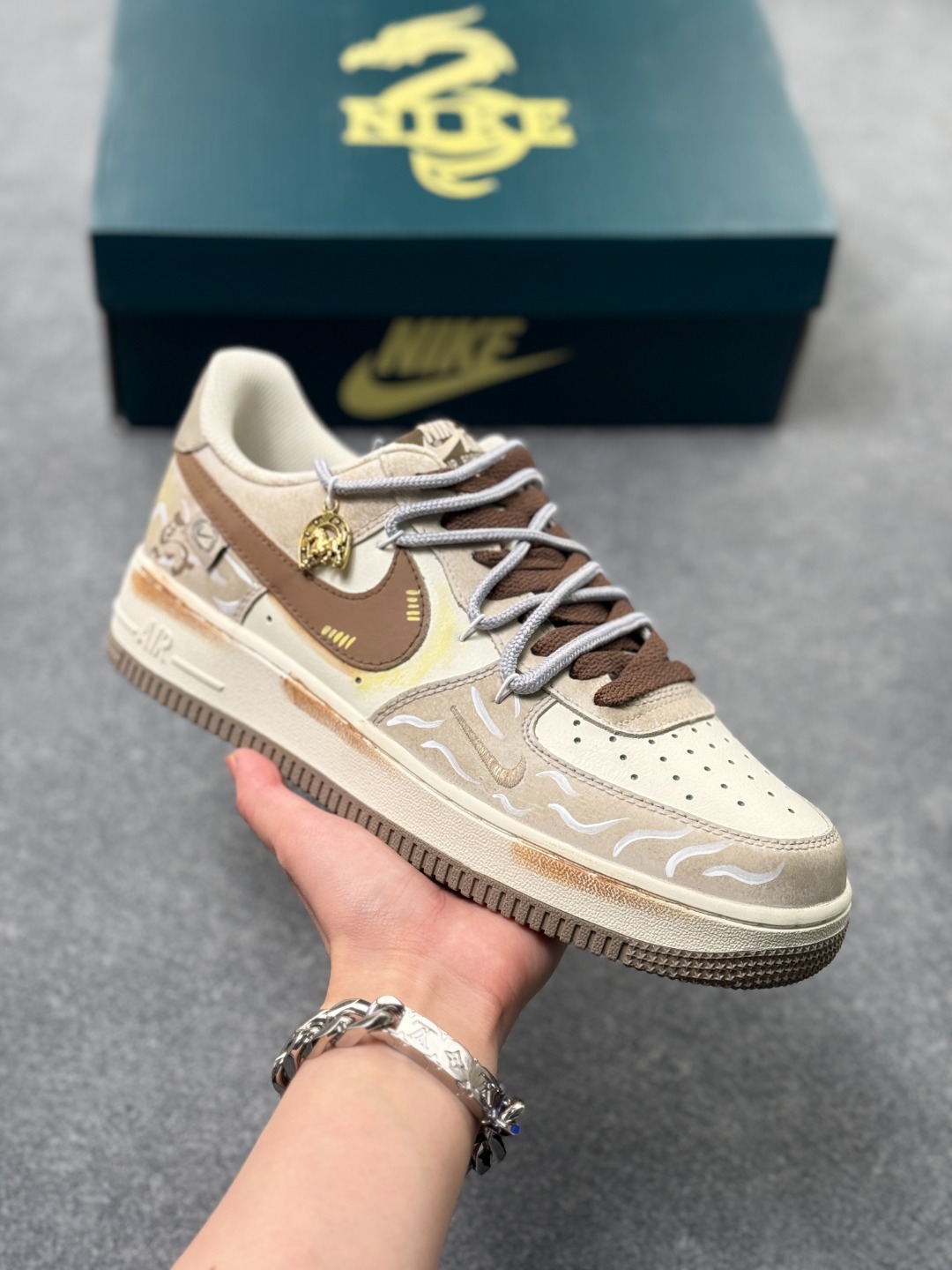 💰220
手绘涂鸦 马年限定“金戈铁马”Nike Air Force 1  “ Armored Steed”空军一号定制板鞋 
 作为 2026 马年限定款，“金戈铁马” 以 “古战意象” 为设计内核，从材质到细节都紧扣主题：鞋身采用雾灰 + 米白做旧混染工艺，模拟古甲胄经沙场摩挲后的斑驳肌理；鎏金勾边的 Swoosh 与金属挂坠，还原兵器鎏金纹饰的质感；鞋侧图腾以 “奔马” 为原型，复刻战马奔腾的劲飒姿态，搭配做旧中底的 “战尘渍迹” 效果
货号：DB3301--818
SIZE: 36 36.5 37.5 38 38.5 39 40 40.5 41 42 42.5 43 44 44.5 45   x69