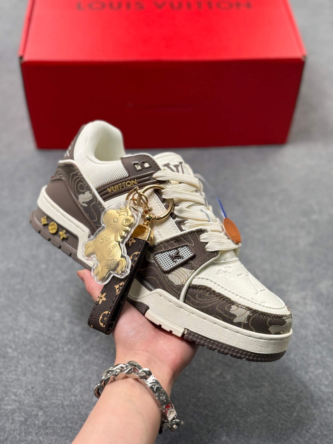 LV TRAINER迷彩马纹(中国红限定礼盒版本-钥匙扣丢失扣20元) 26年限定中国红礼盒及全套包装说明书防尘布袋物件,完美楦型,独家开模定制! trainer这个系列是路易威登融合街头潮流与高级时装的标志性之作.在材料选用上,鞋面采用Monogram印花与Monogram压纹粒面牛皮革的搭配,呈现出独特的复古韵味.荔枝纹粒面头层牛革鞋面,触感细腻且富有韧性,自带自然的皮革纹理,彰显高级质感,为鞋子增添了丰富的层次感.鞋垫采用原版超软乳胶材质,新鞋零磨合不磨脚,软乎乎的皮质包裹感超棒,鞋底则采用橡胶材质,刻有经典的Monogram花卉纹路,不仅防滑,还带走缓震效果还极具设计感.做工方面,TRAINER系列板鞋展现了精湛的工艺水准.鞋头采用圆润设计,原版空胶工艺搭配包边工艺,不仅美观,还能有效防踢蹭.鞋舌、侧面和后部饰有LV字母,侧面还有Vuitton标识,均做工精细,彰显品牌身份.鞋身走线工整均匀,看不到任何多余的线头,皮革的拼接处也处理得极为细腻,体现了我们对细节的极致追求.百搭属性直接封神!配牛仔裤是复古街头风,搭西装裤秒变松弛通勤感,甚至配半身裙都甜妹感拉满,堪称"衣柜万能钥匙".这双集颜值、质感、实穿性于一体的奢牌板鞋! 货号:2A8DM21VL IZE:36 37 38 39 40 41 42 43 44 45(不带半)x45