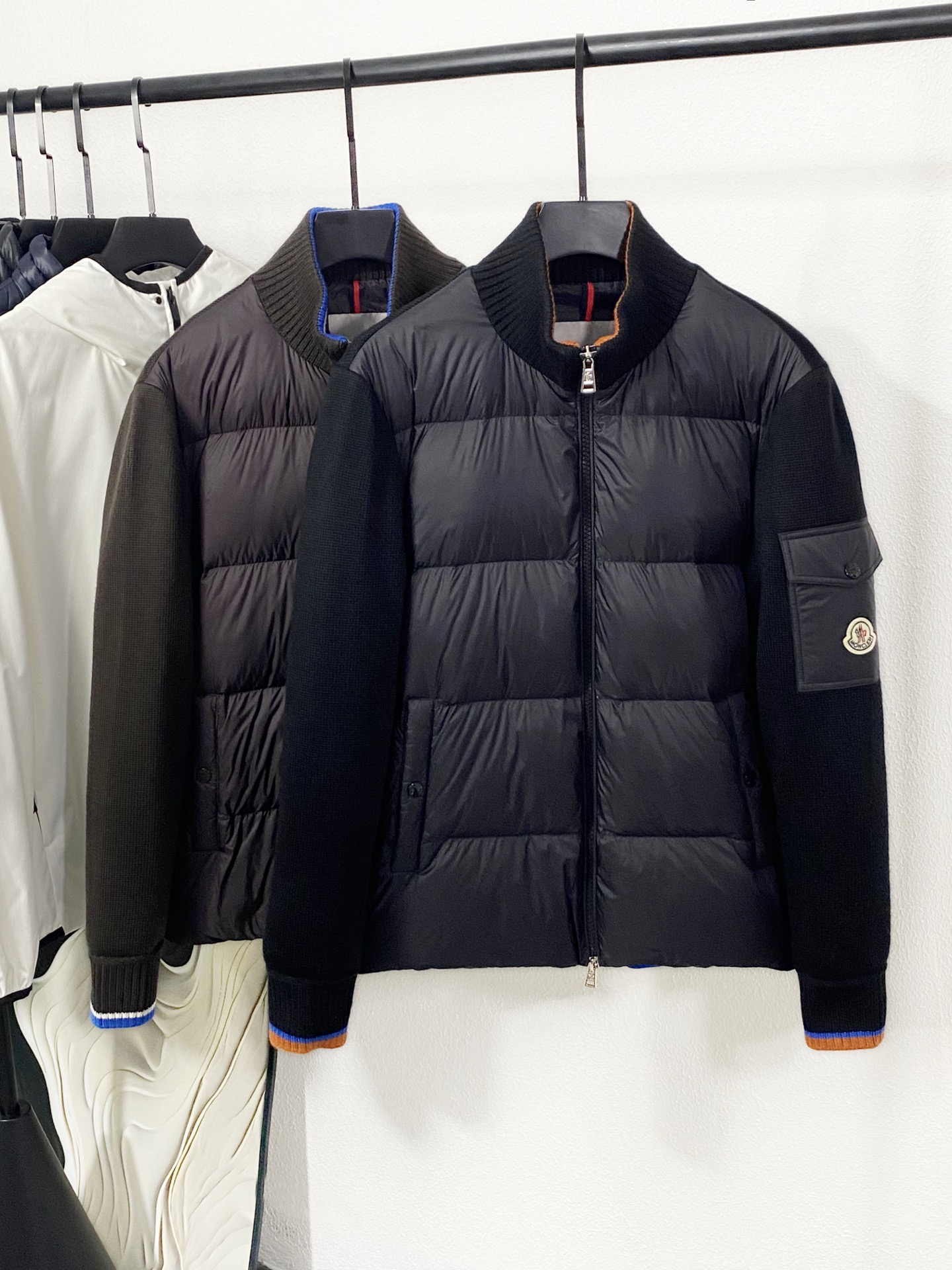 NO:611483,(New product) Moncler/Moncler 25 new autumn and winter new men's patchwork fabric long-sleeved stand-collar down jacket. The left arm of the armband is equipped with Moncler's iconic circular logo. The embroidery process is exquisite, and the red and white brand logo is highly recognizable, which is an intuitive reflection of the brand identity. The front zipper puller is made of metal and is engraved with the Moncler brand's exclusive pattern. It is full of texture and ensures the smoothness and durability of the zipper.  The main down part is made of nylon fabric with a matte texture, with a smooth surface and good windproof performance. The classic quilting process forms a regular grid, which not only fixes the down to prevent it from running away, but also enhances the three-dimensional effect. The sleeves and back of the knitted splicing part are made of black thick-knitted fabric, with clear texture and rich texture. The addition of knitted fabric not only increases the layering of the outfit, but also improves the comfort and breathability of wearing, achieving a combination of down warmth retention and knitting flexibility.  Contrast striped knitted cuffs and the inside of the collar are equipped with contrasting brown and blue stripes, which add vitality and design to the overall pure black tone, and the details highlight fashionable taste. Buttons and pockets The pockets on both sides of the front placket are closed with buttons, and the buttons are printed with the Moncler brand logo, which is consistent with the overall style; there is also a small pocket on the left arm, which has both decorative and practical functions.  The filling is made of 90% white goose down, which has high fluffiness and excellent thermal insulation performance, and can provide the wearer with sufficient warmth in autumn and winter. The lining is also made of nylon fabric, which is smooth to the touch and echoes the texture of the outer fabric, while ensuring the cleanliness and durability of the interior. The stand-up collar is designed in a knitted stand-up collar style, which can fit the neck well, block the intrusion of cold wind, improve the thermal insulation effect, and create a smart wearing style.  The overall style is casual and loose, comfortable and unrestrained, suitable for a variety of body types, and easy to layer inside to meet the multi-layered needs of autumn and winter. This down jacket combines Moncler's classic down technology and innovative fabric splicing design. It not only has professional thermal performance, but also shows a unique style in fashion design. It is a high-quality item that is both practical and trendy in autumn and winter. 48-56  48 shoulder width 47 bust 112 length 64 sleeve length 61 50 shoulder width 48 bust 116 length 65 sleeve length 62 52 shoulder width 49 bust 120 length 66 sleeve length 63 54 shoulder width 50 bust 124 length 67 sleeve length 64 56 shoulder width 51 bust 128 length 68 sleeve length 65,,Moncler,down jacket,alexander wang19860909(新品)Moncler/蒙口 25新品秋冬新品男士拼面料长袖立领羽绒服 袖章左臂设有Moncler标志性的圆形徽标,刺绣工艺精致,红白配色的品牌标识辨识度极高,是品牌身份的直观体现.拉链头前襟拉链头采用金属材质,刻有Moncler品牌专属的图案,质感十足,同时保证拉链使用的顺滑与耐用. 主体羽绒部分采用哑光质感的锦纶面料,表面光滑且具有良好的防风性能,经典的绗缝工艺形成规整的方格,既固定羽绒防止跑绒,又增强了立体感. 针织拼接部分袖子及背部采用黑色粗针针织面料,纹理清晰,富有质感.针织面料的加入不仅增加了穿搭的层次感,还提升了穿着的舒适度与透气性,实现了羽绒保暖性与针织灵活性的结合. 撞色条纹针织袖口和领口内侧设有棕色与蓝色的撞色条纹,为纯黑的整体色调增添了活力与设计感,细节处彰显时尚品味. 纽扣与口袋前襟两侧的口袋采用纽扣闭合设计,纽扣上印有Moncler品牌标识,与整体风格保持一致；左臂还有一个小口袋,兼具装饰与实用功能. 填充物采用90白鹅绒填充,蓬松度高,保暖性能优异,能在秋冬季节为穿着者提供充足的温暖. 里料内里同样使用锦纶面料,触感顺滑,与外层面料的质感形成呼应,同时保证了内部的整洁与耐用. 立领设计针织立领款式,能够很好地贴合颈部,阻挡寒风侵入,提升保暖效果,同时塑造出干练的穿搭风格. 整体版型属于休闲宽松版型,穿着舒适无束缚,适合多种身材,且便于内搭叠穿,满足秋冬季节的多层次穿搭需求. 这款羽绒服融合了Moncler的经典羽绒技术与创新的面料拼接设计,既具备专业的保暖性能,又在时尚设计上展现出独特的风格,是秋冬季节兼具实用性与潮流感的优质单品.48-56 48肩宽47胸围112衣长64袖长61 50肩宽48胸围116衣长65袖长62 52肩宽49胸围120衣长66袖长63 54肩宽50胸围124衣长67袖长64 56肩宽51胸围128衣长68袖长65,,Moncler,down jacket,alexander wang,Men's clothing