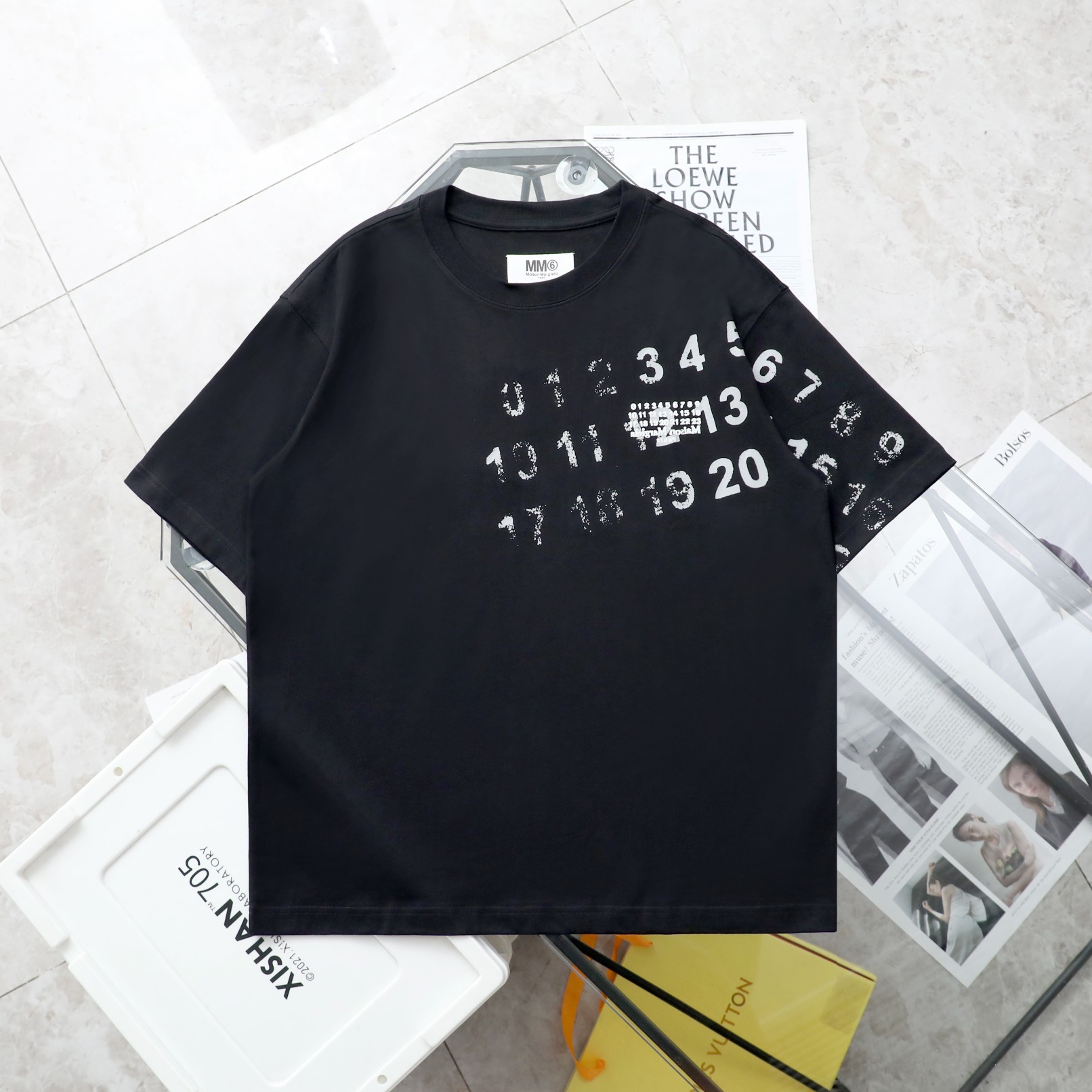 【纯原臻品 顶级复刻】\nMaison Margiela/马吉拉模糊数字印花短袖T恤\n- 款号：0\n- 颜色：黑色 白色  \n- 购入原版开模打造，全套定制辅料，细节决定成败\n- 马丁·马吉拉（Martin Margiela，年月日－）是比利时服装设计师，出生于比利时亨克。和比利时前卫风格-安特卫普六君子皆为安特卫普皇家艺术学院毕业学生。个人品牌为 Maison Martin Margiela Maison为（法文'家'的意思），并于ZD年正式宣布推出[]他个人品牌。于年月正式更名为Maison Margiela。[]\n- 面料：ZB克定制双纱高密度纯棉面料\n- 工艺: 整件衣服采用精密压花工艺\n- 辅料：全套马吉拉原版专柜辅料\n- 男女同款均可驾驭\n- 尺码：S～XL\nS: 衣长 胸围???????????? 肩宽 袖长\nM: 衣长 胸围肩宽 袖长\nL: 衣长  