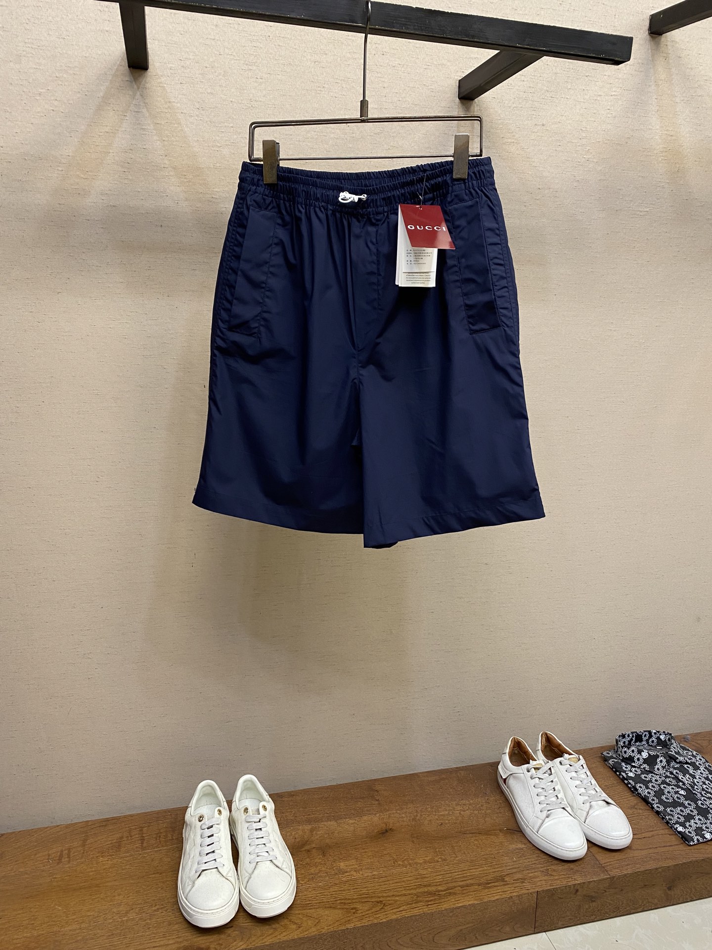 NO:437093,Gucci decorative cotton poplin shorts Fabric selection Use cotton fiber to weave twice the warp yarn to form a cotton poplin fabric with fine surface and uniform rhombus grain texture, smooth and slightly glossy texture. Pure cotton material absorbs moisture and breathable, and is not easy to stuffy. The high-density structure strengthens its wear resistance and has good wrinkle resistance. Process 1 Carve the adhesive strips through a high-precision laser beam, and ensure the edge accuracy of ±0.1 mm through a dynamic focusing system, thus forming a high-precision letter LOGO. Then use a hot press (temperature controlled at about 150°, pressure of 5kg/CM) to bond the adhesive strips to the fabric, and finally tie them in the same color on the edge, firmly decorate them on the back patch pocket. Process 2  The elastic waist is built-in elastic silicone ribs, which fit different waist shapes. The external is equipped with adjustable drawstring buckles, which are fixed with a customized buckle. The elasticity can be adjusted with one hand, taking into account practicality and aesthetics. Size S-XL, gucci, shorts, alexander wang19860909Gucci饰标棉府绸短裤 面料选择 选用棉纤维以经纱两倍于纬纱的平纹织法,形成表面细密、均匀的菱形颗粒纹理,触感光滑且略带光泽感的棉府绸面料.纯棉材质吸湿透气,不易闷热.高密度的结构强化其耐磨性同时又具有良好的抗皱性. 工艺1 通过高精度的激光束对胶条进行雕刻,通过动态聚焦系统确保边缘精度达±0.1毫米,从而形成高精准度的字母LOGO.再运用热压机（温度控制在150°左右,压力5kg/CM）将胶条与面料黏合,最后在边缘处车上同色系线,牢固的饰于后贴袋之上 工艺2 松紧腰围内置弹力硅胶筋,贴合不同腰型,外部搭配可调节抽绳栓扣,以定制扣头固定,单手即可微调松紧,兼顾实用性和美观性. 尺码S-XL,,gucci,shorts,alexander wang,Men's clothing