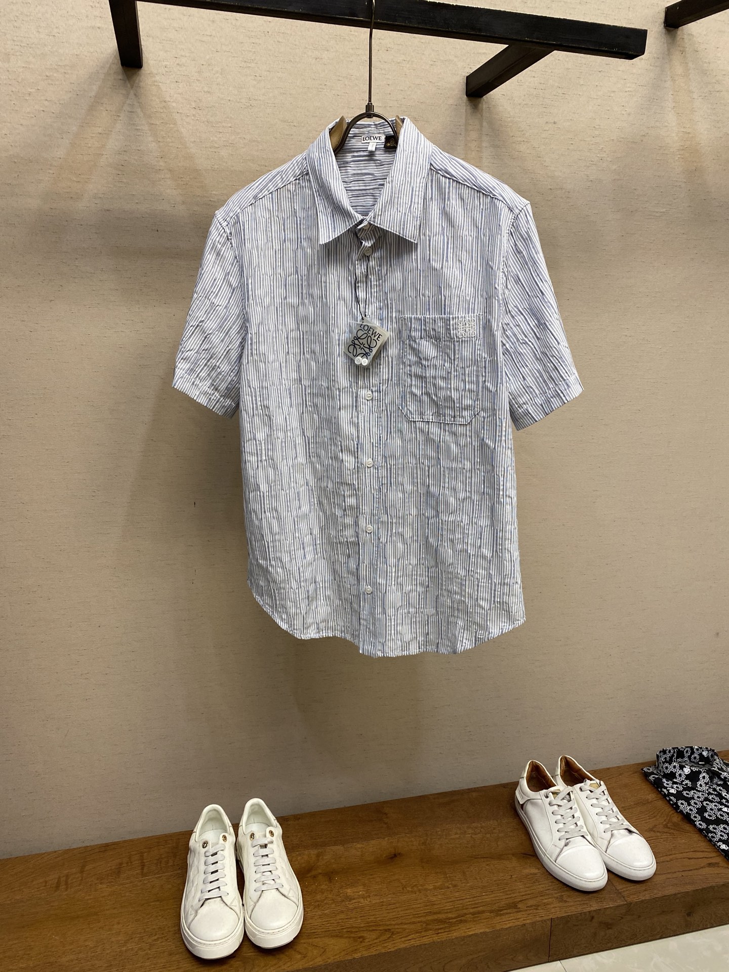 NO:418334,Loewe, striped wavy texture short-sleeved shirt fabric selection. Triple-gold proportion cotton blend fabric is used. The cotton fiber has the characteristics of natural skin-friendly, soft and strong water absorption. Its structural characteristics retain the breathability of the fabric and reduce the sultry feeling. The blessing of a small amount of nylon and spandex accelerates the diffusion of moisture through the capillary effect to avoid the wet and sticky feeling of pure cotton. At the same time, it significantly improves the stretchability and resilience, takes into account the pattern retention and reduces the shrinkage rate. Process 1: During the knitting process, the spandex yarn guide is programmed to intermittently woven into the back of the fabric. Due to the shrinkage of spandex, it forms a 'wavy' wrinkle texture, and the unwoven spandex area maintains the original shape of the fabric. It not only retains the frontal visual neatness, but also transmits a visual three-dimensional feeling through the reverse shrinkage force. Process 2 The breast patch pocket is made of thousands of needles with high-precision Anagram embroidery through the advanced computer control system and precise mechanical parts of the embroidery machine. Size S-XL, loewe,shirts,T-shirt, gold,alexander wang19860909Loewe,条纹波浪纹理短袖衬衫 面料选择 选用三重黄金比例棉质混纺面料,棉纤维具有天然亲肤、柔软、吸水性强等特点.其结构特性保留了面料的透气性,减少闷热感.少量锦纶和氨纶的加持通过毛细效应加速水分扩散,避免纯棉的湿粘感,同时又显著提升了伸张性和回弹性,兼顾保型性,降低缩水率. 工艺1: 在针织过程中,通过编程控制氨纶导纱器,使其间歇性织入面料反面,因氨纶收缩形成‘波浪状’褶皱纹理,未织入氨纶区域保持面料原状.既保留了正面视觉整洁度,又通过反向收缩力传递视觉立体感. 工艺2 胸贴袋片处通过绣花机先进的计算机控制系统和精密的机械部件形成上千针的高精度Anagram刺绣. 尺码S-XL,,loewe,shirts,T-shirt,gold,alexander wang,Men's clothing