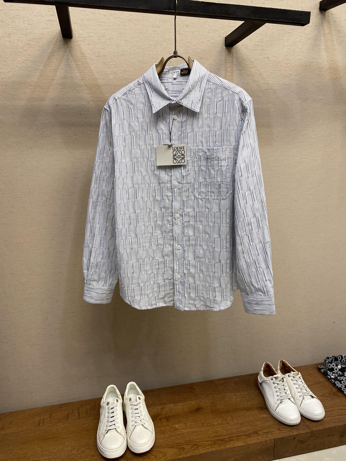 NO:505647,Loewe, striped wavy texture long-sleeved shirt fabric selection. Triple-gold proportion cotton blend fabric is used. The cotton fiber has the characteristics of natural skin-friendly, soft and strong water absorption. Its structural characteristics retain the breathability of the fabric and reduce the sultry feeling. The blessing of a small amount of nylon and spandex accelerates moisture diffusion through capillary effect to avoid the wet and sticky feeling of pure cotton. At the same time, it significantly improves stretchability and rebound, takes into account the pattern retention and reduces the shrinkage rate. Process 1: During the knitting process, the spandex yarn guide is programmed to intermittently woven into the back of the fabric. Due to the shrinkage of spandex, it forms a 'wavy' wrinkle texture, and the unwoven spandex area maintains the original shape of the fabric. It not only retains the frontal visual neatness, but also transmits a visual three-dimensional feeling through the reverse shrinkage force. Process 2 The breast patch pocket is made of thousands of needles with high-precision Anagram embroidery through the advanced computer control system and precise mechanical parts of the embroidery machine. Size S-XL, loewe,shirts, gold, alexander wang19860909Loewe,条纹波浪纹理长袖衬衫 面料选择 选用三重黄金比例棉质混纺面料,棉纤维具有天然亲肤、柔软、吸水性强等特点.其结构特性保留了面料的透气性,减少闷热感.少量锦纶和氨纶的加持通过毛细效应加速水分扩散,避免纯棉的湿粘感,同时又显著提升了伸张性和回弹性,兼顾保型性,降低缩水率. 工艺1: 在针织过程中,通过编程控制氨纶导纱器,使其间歇性织入面料反面,因氨纶收缩形成‘波浪状’褶皱纹理,未织入氨纶区域保持面料原状.既保留了正面视觉整洁度,又通过反向收缩力传递视觉立体感. 工艺2 胸贴袋片处通过绣花机先进的计算机控制系统和精密的机械部件形成上千针的高精度Anagram刺绣. 尺码S-XL,,loewe,shirts,gold,alexander wang,Men's clothing