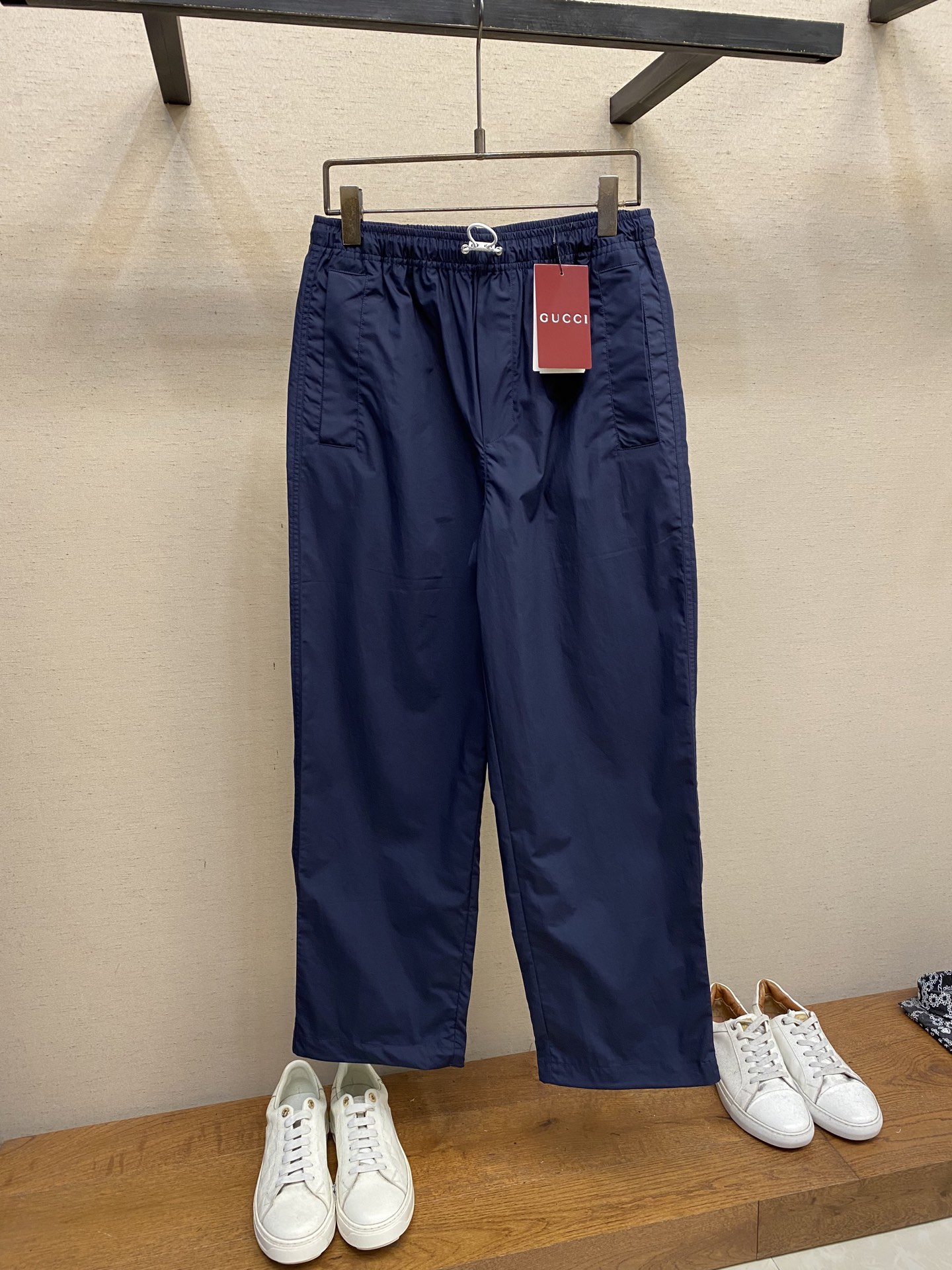 NO:455823,Gucci decorative letter logo cotton poplin trousers Fabric selection Use cotton fiber to weave with double the warp yarn to form a fine and uniform rhombus grain texture with a smooth and slightly glossy texture. Pure cotton material absorbs moisture and breathable, and is not easy to stuffy. The high-density structure strengthens its wear resistance and has good wrinkle resistance. Process 1 Carve the adhesive strips through a high-precision laser beam, and ensure the edge accuracy of ±0.1 mm through a dynamic focusing system, thus forming a high-precision letter LOGO. Then use a hot press (temperature controlled at about 150°, pressure of 5kg/CM) to bond the adhesive strips to the fabric, and finally tie them in the same color on the edge, firmly decorate them on the back patch pocket. Process 2  The elastic waist is built-in elastic silicone ribs, which fit different waist shapes. The external is equipped with adjustable drawstring buckles, which are fixed with a customized buckle. The elasticity can be adjusted with one hand, taking into account practicality and aesthetics. Size S-XL, gucci, alexander wang19860909Gucci饰字母徽标棉府绸长裤 面料选择 选用棉纤维以经纱两倍于纬纱的平纹织法,形成表面细密、均匀的菱形颗粒纹理,触感光滑且略带光泽感的棉府绸面料.纯棉材质吸湿透气,不易闷热.高密度的结构强化其耐磨性同时又具有良好的抗皱性. 工艺1 通过高精度的激光束对胶条进行雕刻,通过动态聚焦系统确保边缘精度达±0.1毫米,从而形成高精准度的字母LOGO.再运用热压机（温度控制在150°左右,压力5kg/CM）将胶条与面料黏合,最后在边缘处车上同色系线,牢固的饰于后贴袋之上 工艺2 松紧腰围内置弹力硅胶筋,贴合不同腰型,外部搭配可调节抽绳栓扣,以定制扣头固定,单手即可微调松紧,兼顾实用性和美观性. 尺码S-XL,,gucci,alexander wang,Men's clothing