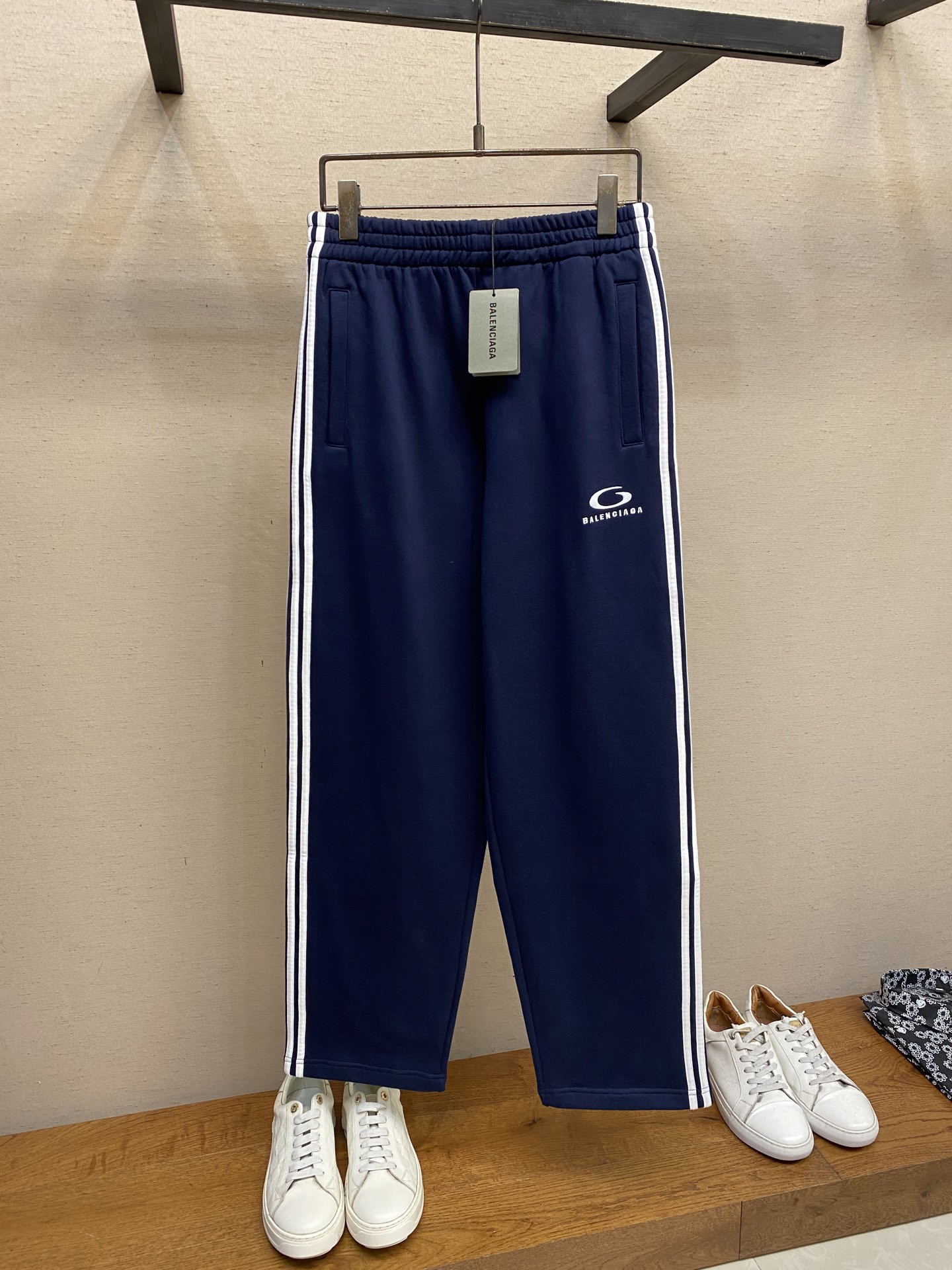 NO:528875,Balenciaga, embroidered lace-edged sports pants Fabric selection A single-sided fish scale fabric woven with cotton as the base. The front is a smooth knitted surface. The touching surface is formed by the floating thread knitting technology of the knitting machine to form a three-dimensional loop, which increases the fluffy feeling and is delicate at the same time. The loop structure absorbs a large amount of water and evaporates quickly, and it is not easy to deform loosely after washing multiple times. Process 1 Use 3000 stitches of imported embroidery machine + with loop sports icon embroidery on the front side of the thigh. The double-axis linear guide drives the embroidery frame, and the frame shift accuracy can reach 0.01mm/P, ensuring the precise positioning of the embroidery pattern. Process 2 The trim is accurately positioned along the waist to the foot, ensuring symmetry and overall smoothness. Before formal sewing, extremely fine and sparse seams are used for pre-fixation. This step is crucial to prevent the trim from sliding, twisting or wrinkling during the sewing process, ensuring the final stitch is straight and perfect.  Process 3 Through active intervention in the shrinkage potential of cotton knitted surfaces, the fabric has achieved a leap from easy to change to stable, improving dimensional stability, and not easily deforming or wrinkling. Size S-XL, balenciaga, alexander wang19860909Balenciaga、刺绣饰边运动裤  面料选择 采用棉为基底编织而成的单面鱼鳞布面料,正面为平滑的针织面,触肤面通过针织机的浮线编织技术形成立体的毛圈,增加蓬松感, 同时触感细腻.毛圈结构吸水量大且蒸发快,多次洗涤不易松散变形. 工艺1 通过进口绣花机3000针+在大腿前侧饰以loop sports icon刺绣.双轴直线导轨驱动绣框,移框精度可达0.01mm/P,确保刺绣图案精准定位. 工艺2 饰条沿腰部至脚口处指定轮廓精准定位,确保对称性与整体流畅度. 在正式缝纫前,采用极细疏缝线迹进行预固定.此步骤至关重要,防止饰条在缝制过程中滑动、扭曲或起皱,保证最终线迹平直完美. 工艺3 通过主动干预棉针织面收缩潜能,实现了面料从易变到稳定的跨越,提升了尺寸稳定性,同时不易变形,褶皱. 尺码S-XL,,balenciaga,alexander wang,Men's clothing