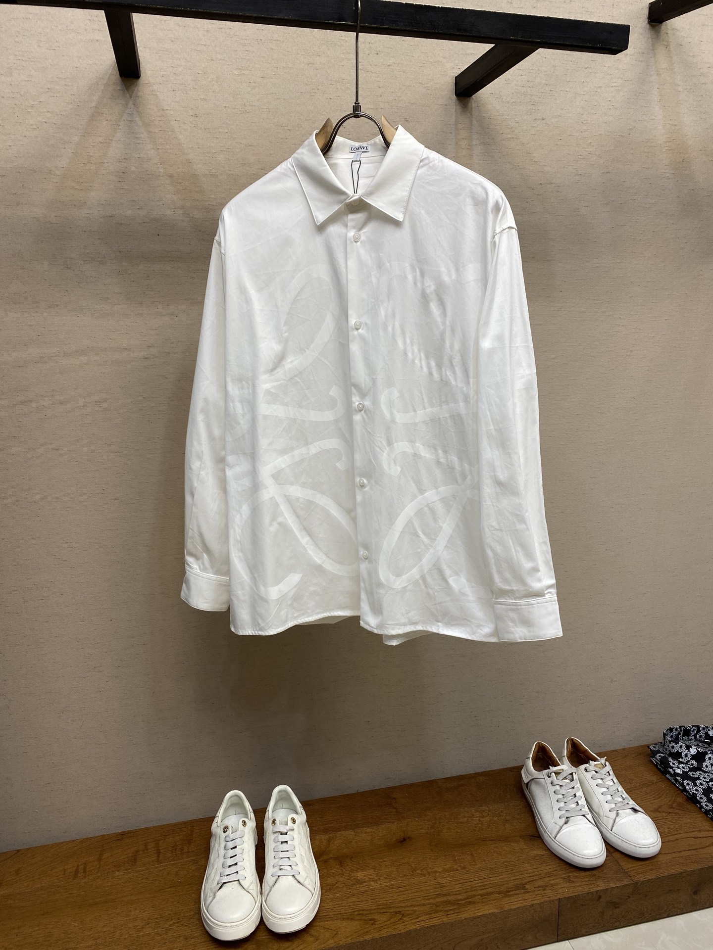 NO:524564,Loewe, dark flower logo lapel shirt is available for sale in white and black original, 800 yuan; light cotton poplin shirt, chest with unprinted dark flower pattern, conventional style, standard length, classic collar, front button closure, button cuffs, full set of auxiliary materials equipped # light cotton poplin shirt fabric Poplin is a classic cotton fabric, characterized by large differences in warp and weft density, forming a delicate diamond-shaped grain texture. This structure not only gives the fabric a refreshing and breathable feeling, but also ensures that its texture is light but slim and crisp, avoiding the disadvantages of ordinary thin cotton easily collapse, perfectly supporting the neat pattern of the shirt, while maintaining the unique skin-friendly comfort of cotton. # chest with unprinted dark flower pattern  The chest is decorated with a printing process printing; the printing is a special process, which exposes the light-colored pattern of the original embryo cloth by etching through the dyed base cloth. This makes the Anagram logo not simply cover the fabric, but blends with the fabric, with a flat and trace-free touch, presenting a low-key and high-end matte effect. # Precise cut version The layout and design shirts use a loose version of standard length; precise cut version. It is not too loose and does not deliberately slim, aiming to create a clean and neat outline, and is extremely inclusive for the body shape. The standard length ensures that the hem can be properly tied into the trousers or hang naturally, meeting the needs of formal and casual wear. Size XS-L (36, 37, 38, 39),,loewe,shirts,alexander wang19860909Loewe、暗花标识翻领衬衫 发售色系白色、黑色 原,800购买；轻盈棉质府绸衬衫、胸前饰有拔印暗花图案、常规版型,标准长度、经典衣领、正面纽扣开合、纽扣袖口、全套辅料配备 # 轻盈棉质府绸衬衫面料 府绸是一种经典的棉织物,其特点是经纬纱密度差异大,形成细腻的菱形颗粒感肌理.这种结构不仅赋予面料清爽透气的穿着感,更确保了其质地轻薄却骨感挺括,避免了普通薄棉易软塌的缺点,完美承托起衬衫的利落版型,同时保持了棉独有的亲肤舒适性. # 胸前饰有拔印暗花图案 胸前饰有拔印工艺印花；拔印是一种特殊工艺,通过蚀穿染色底布,露出原胚布的浅色图案.这使得Anagram标志并非简单地覆盖于面料之上,而是与面料融为一体,触感平整无痕,呈现出一种低调而高级的哑光效果. # 对版精准剪裁版型 版型与设计衬衫采用标准长度的宽松版型；对版精准剪裁.不过分宽松也不刻意修身,旨在打造干净利落的轮廓,对体型都具有极高的包容性.标准长度确保下摆能够妥帖地束入裤装或自然垂落,满足正式与休闲等多种穿搭需求. 尺码XS-L（36,37,38,39）,,loewe,shirts,alexander wang,Men's clothing