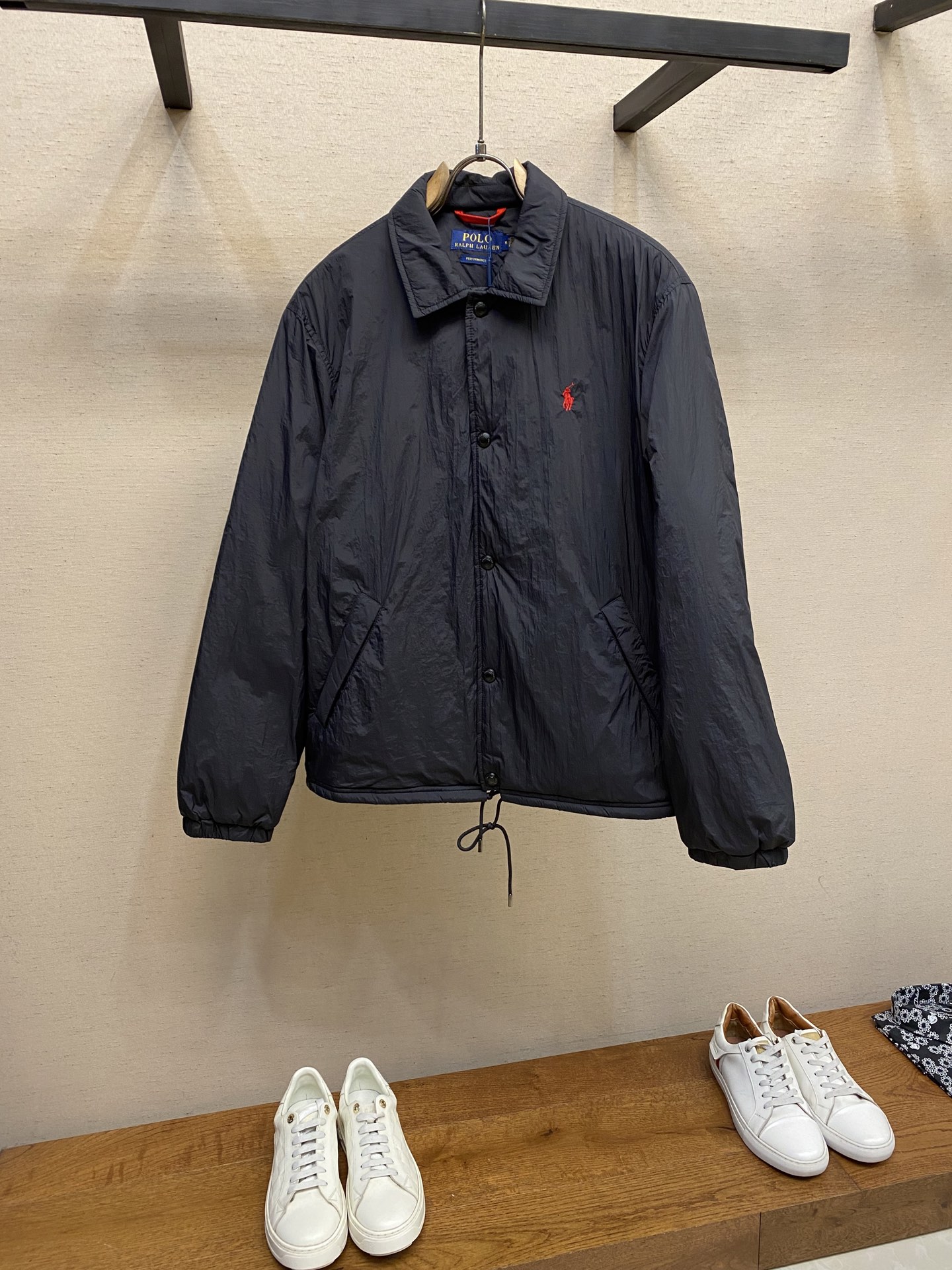 NO:623986,Ralph Lauren's red label light cotton clothing combines pragmatism and classic texture in fabric procurement. The material is high-density nylon taffeta. The characteristic density is about 210T-300T. The surface is smooth and slightly matte. It has excellent windproof and waterproof performance (with DWR water-repellent treatment). It is wrinkle-resistant and easy to care for. It is in line with the positioning of American casual 'durable and practical'. The color is classic dark black, using the vat dyeing process (the dye penetrates into the fiber), and the color fastness reaches ISO  Level 4 or above, to avoid fading or discoloration after washing. 2. Lining material: Light and thin cotton-polyester blended lining (65 Polyester + 35 Cotton), which can reduce friction between the fabric and inner clothing and improve the smoothness of wearing; the blended material has both breathability and durability, and avoids the stuffy feeling of pure nylon lining. Style and tailoring process: classic coach jacket (Coach)  Jacket) loose version, slightly dropped shoulder line (shoulder width is 1-2cm wider than the standard version), length to the hips, sleeves with slightly tapered straight sleeves, taking into account freedom of movement and casual style. Embroidery technology: left chest Polo horse logo flat satin stitch embroidery (satin embroidery),  The embroidery thread is made of polyester high color fastness embroidery thread (the color number is consistent with the brand's standard red color card), the stitch density is 12-15 stitches/cm, the outline of the horse mark is clear, and the details of the rider and horse are burr-free. The embroidery positioning is accurately positioned through the template (12cm from the collar and 8cm from the placket) to ensure left and right symmetry and centering.  The seams of the topstitched body are made of double-needle flat seams (needle distance 3cm/10 needles), the stitches are flat and straight, the stitching color is dark black (the same color as the fabric), and the stitch width is 0.5cm, which enhances firmness while forming simple decorative lines. 1. Main body splicing  The front placket is spliced with the body. The placket is spliced with double-layer folding + flat seams, with a thickness of about 0.3cm to ensure that it is not easily deformed when the buttons are fixed; the edges of the placket are cut with a hot knife to avoid rough edges. The armholes of the sleeves and the body are spliced with round head buttonholes and flat seams. After splicing, the armholes have a natural curvature and no sense of tightness during movement; the height of the sleeves is about 8-10cm, which is in line with the loose characteristics of casual jackets.  The main button is a black urea resin button with a matte surface. The buttonhole is a hand-made keyhole (6 strands of cotton thread, keyhole density 8 stitches/mm), and the edge of the eyelet is smooth without burrs. The first button on the collar is a hidden button (diameter 12mm), which prevents the collar from opening and improves the neatness of the dress. Sizes S-XL,,coach,loro piana,jackets & coats,alexander wang19860909Ralph Lauren拉夫劳伦红标轻薄棉服 面料采购实用主义与经典质感的结合 材质高密度尼龙塔夫绸 特性密度约210T-300T,表面光滑微哑光,防风防水性能优异（经DWR防泼水处理）,抗皱性强且易打理,符合美式休闲“耐穿实用”的定位. 颜色经典藏黑色,采用缸染工艺（染料渗透纤维内部）,色牢度达ISO 4级以上,避免洗涤后褪色或串色. 2.衬里面料 材质轻薄棉涤混纺里布（65 Polyester + 35 Cotton） 作用减少面料与内搭衣物的摩擦,提升穿着顺滑度；混纺材质兼顾透气性与耐用性,避免纯尼龙内衬的闷热感. 版型与剪裁工艺 版型经典教练夹克（Coach Jacket）宽松版型,肩线微落（肩宽比标准版型宽1-2cm）,衣长至臀部,袖型为微锥度直筒袖,兼顾活动自由度与休闲风格. 刺绣工艺 左胸Polo马标平面 satin stitch 刺绣（缎面绣）, 绣线采用涤纶高色牢度绣线（色号与品牌标准红色色卡一致）,线迹密度12-15针/cm,马标轮廓清晰,骑手、马匹细节无毛刺. 刺绣定位通过模板精准定位（距离领口下12cm,距门襟8cm）,确保左右对称且居中. 明线工艺衣身接缝处采用双针平缝（针距3cm/10针）,线迹平整笔直,缝线颜色为藏黑色（与面料同色）,线迹宽度0.5cm,增强牢固度的同时形成简洁的装饰性线条. 1.主体拼接 前襟与衣身拼接门襟处采用双层对折+平缝拼接,厚度约0.3cm,确保纽扣固定时不易变形；门襟边缘用热切刀切割,避免毛边. 袖片与衣身拼接袖窿处采用圆头锁眼机锁边+平缝拼接,拼接后袖窿弧度自然,活动时无紧绷感；袖山高度约8-10cm,符合休闲夹克的宽松特性. 主纽扣黑色尿素树脂扣,表面哑光处理,纽扣孔为手工锁眼（6股棉线,锁眼密度8针/mm）,孔眼边缘光滑无毛边. 领部纽扣领口第一颗纽扣为隐藏式暗扣（直径12mm）,防止领口敞开,提升穿着整洁度. 尺码S-XL,,coach,loro piana,jackets & coats,alexander wang,Men's clothing