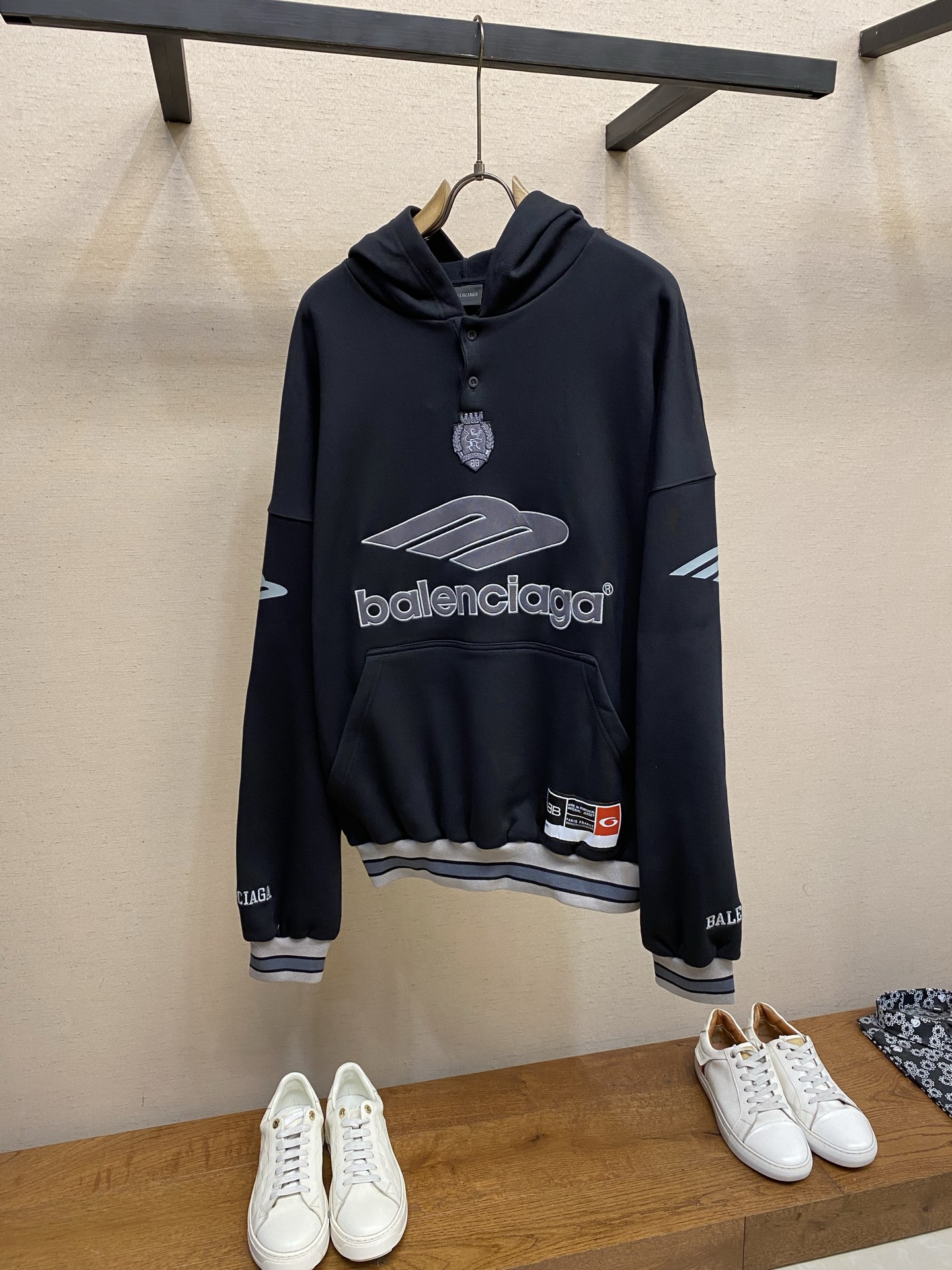 NO:655869,Balenciaga team series hooded sweatshirt. Original purchase, 500; terry bottom sweatshirt fabric, decorated with 3B art patch embroidery on the front and back, decorated with elastic eco-friendly glue printing, no drawstring hood, Polo button collar, dropped shoulders, 1 kangaroo pocket on the front, gathered cuffs and waist, full set of accessories # terry bottom sweatshirt fabric  It adopts a composite sweatshirt fabric structure with a 26-count double yarn top layer and a terry base, with a weight of 380g/㎡. It is a classic heavy-weight high-end sweatshirt fabric. The 26-count double yarn forms a smooth, delicate and strong outer surface of the fabric, ensuring good appearance and color fastness; the 10-count terry base is woven to form a loose  Thick coils, after being raised or brushed, form a layer of dense and soft velvet on the inside of the fabric. This structure makes the sweatshirt have a crisp and skin-friendly texture on the outside and a warm, skin-friendly feel on the inside. The 380g weight gives the garment excellent drape and wrinkle resistance, making its silhouette full and not easy to collapse.  The color-blocked striped flat machine cuffs and hem are spliced with color-blocked rib strips to form a ring-shaped stripe similar to sportswear. Functionally, it tightens the cuffs to prevent drafts and streamline the lines; it visually echoes the color-blocked V-neck, strengthening the overall sense of movement and design unity. # Combination of appliqué embroidery and glue printing 3B on the front and back  Patch embroidery pre-cuts the pattern on fabrics of different materials or colors and then covers it on the body of the body. Finally, it is fixed with high-density embroidery thread to outline the internal details. Its function is to create a pattern with bright colors, strong texture contrast, three-dimensional effect and durability. The edges of the pattern are strong and not easy to wear.  Elastic eco-friendly glue printing uses a process of screen-printing special elastic glue on the sleeves to produce brightly colored patterns with a slight coating feel. The elastic glue ensures that the printed area can stretch with the fabric without cracking. It forms a flat and one convex texture contrast with the three-dimensional effect of the patch embroidery, which increases the interest and complexity of the design. # The fusion of POLO collar and drawstring-less hood  The POLO button collar is embedded in the front neckline of the hooded sweatshirt with a half-open placket design with several buttons. Its function is to break the monotony of the traditional pullover sweatshirt, provide a more flexible way to put on and take off the collar and shape the collar, give the sweatshirt a touch of retro sports elegance, and enhance the decorative level of the front chest area.  The drawstringless hooded hat removes the common functional drawstring, and its function is to pursue minimalist and smooth contours, making the overall appearance cleaner and neater. This requires that the hat itself must be cut very accurately to ensure that it can have a well-fitting wrapping feeling behind the head without relying on the drawstring. Sizes XS-L,,balenciaga,hoodie,sweatshirts,hats,alexander wang19860909Balenciaga 队系列连帽卫衣 原,500购买；毛圈底卫衣面料、正面和背面饰以3B艺术贴布刺绣工艺、饰有弹力环保胶浆印花、无抽绳兜帽、Polo纽扣领襟、落肩、正面1个袋鼠式口袋、缩褶袖口和腰围、全套辅料配备 # 毛圈底卫衣面料 采用26支双纱面层支纱毛圈底的复合卫衣面料结构,克重为380g/㎡.经典的重磅高端卫衣面料,26支双纱构成了面料光滑、细腻且坚固的外表面,确保良好的外观和色牢度；10支纱毛圈底则通过织造形成松厚的线圈,经过起绒或刷绒处理后,在面料内侧形成一层浓密柔软的绒毛.这种结构使得卫衣同时具备外部的挺括骨感与内部的温暖亲肤触感,380g的克重赋予了成衣优异的垂坠感和抗皱性,使其廓形饱满不易软塌. 拼色条纹扁机收口袖口及下摆采用拼色的罗纹条带拼接,形成类似运动服的环状条纹.在功能上收紧袖口,防止灌风并利落线条；在视觉上与拼色V领形成呼应,强化了整体的运动感和设计统一性. # 贴布绣与胶浆印花的结合 正面和背面的3B 贴布刺绣将图案在不同材质或颜色的布料上预先裁剪成型贴布,然后将其覆盖在衣身上,最后用高密度绣线锁边固定并勾勒内部细节.其作用在于创造色彩鲜明、质感对比强烈且极具立体感和耐用性的图案,图案边缘牢固,不易磨损. 弹力环保胶浆印花将特制的弹性浆料通过网版印刷在袖部的工艺,色彩鲜艳且具有轻微涂层感的图案.弹力浆料保证了印花区域能随面料一起拉伸而不开裂.与贴布绣的立体感形成一平一凸的质感对比,增加了设计的趣味性和复杂度. # POLO领与无抽绳连帽的融合 POLO纽扣领襟在连帽卫衣的前领口处,嵌入了带有数颗纽扣的半开襟设计.其作用在于打破了传统套头卫衣的单调,提供了更灵活的穿脱方式与领部造型选择,赋予了卫衣一丝复古运动的优雅感,并增强了前胸区域的装饰层次. 无抽绳兜帽帽子去掉了常见的功能性抽绳,其作用在于追求极简、流畅的轮廓线条,使整体外观更显干净利落.这要求帽子本身的剪裁必须非常精准,以确保不依赖抽绳也能拥有合体的头后包裹感. 尺码XS-L,,balenciaga,hoodie,sweatshirts,hats,alexander wang,Men's clothing