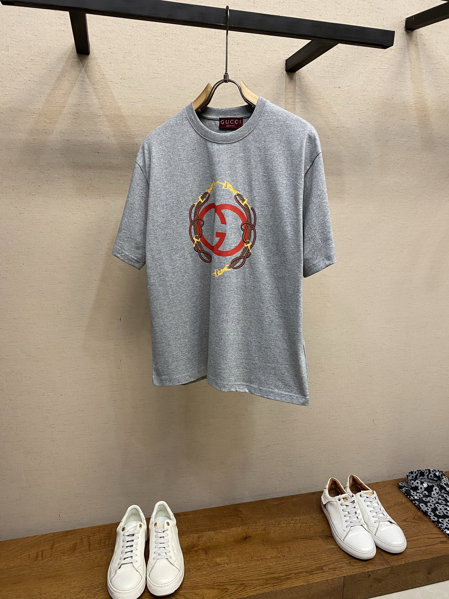 NO:685935,Gucci GU bridle webbing round neck short sleeves. Available in gray and white. Original purchase; fine velvet knitted cotton fabric, interlocking double G bridle print, round neck short sleeves, regular fit, full set of accessories. #Fine velvet knitted cotton fabric 5S special woven compact fine velvet knitted cotton, weight 230g/㎡; paired with 32S high count and high weight 1x1 rib, weight 340g/㎡. The rib is used on the collar, ensuring excellent elastic recovery and deformation resistance of the collar. The fabric uses compact spinning technology in the spinning process, which significantly reduces yarn hairiness and makes the fabric structure more beautiful. Dense, smoother surface, and better pilling resistance; fine velvet knitted fabric means that the fabric has been lightly sanded or raised. The feel is close to extremely fine suede; soft and waxy skin-friendly touch. The weight of 230g is medium to heavy, which gives the T-shirt good stiffness and drape, ensuring the texture of the garment and the silhouette that is not easy to collapse. # Interlocking double G reins printing The pattern adopts an environmentally friendly elastic glue printing process. The special environmentally friendly water-based elastic glue is transferred to the surface of the fabric through a fine silk screen, and then baked and solidified at high temperature. Its elastic properties ensure that the printed pattern can stretch with the fabric without cracking, and has excellent durability; the printed area presents a semi-matte uniform coating effect with high color saturation. It feels soft to the touch without obvious film hardness, maintaining the original breathability and comfort of the fabric. # Round neck straight version. The straight and loose cut leaves allowances under the armpits and side seams through three-dimensional tailoring to achieve zero restriction of movement. The dropped shoulder design weakens the shoulder lines and enhances the casual atmosphere. All seams are embedded with elastic molding strips, and the cuffs and hems adopt double-needle and double-thread seaming technology to ensure that the version remains in its original state after multiple washings. Sizes XS-L,, gucci, T-shirt, tees, t-shirt,19860909Gucci GU 缰绳织带圆领短袖 发售色系灰色、白色 原购买；细绒针织棉面料、互扣式双G缰绳印花、圆领短袖、常规版型、全套辅料配备 # 细绒针织棉面料 5S特纺紧密细绒针织棉,克重230g/㎡；搭配32S高支高克重1x1罗纹,克重340g/㎡.罗纹用于领口,确保了领型极佳的弹性恢复力和抗变形能力.面料在纺纱环节采用了紧密纺技术,显著减少了纱线毛羽,使得面料结构更密实、表面更光洁、抗起球性更佳；细绒针织指面料经过了轻微的磨毛或起绒处理.手感接近极细的绒面；柔软、丰糯的亲肤触感,230g的克重属于中等偏重磅,赋予了T恤良好的挺括度和垂坠感,确保了成衣的质感和不易软塌的廓形. # 互扣式双G缰绳印花 图案采用环保弹力胶浆印花工艺.将特制的环保水性弹力浆料通过精细的丝网网版,转印到面料表面,然后经过高温烘烤固化.其弹力特性确保了印花图案能够随面料一起拉伸而不开裂,耐用性极佳；印花部位呈现半哑光的均匀涂层效果,色彩饱和度高.触感柔软无明显胶膜硬块,保持了面料原有的透气性和舒适度. # 圆领直筒版型 直筒宽松剪裁通过立体剪裁在腋下与侧缝预留余量,实现活动零束缚.落肩设计弱化肩部线条,强化休闲氛围.所有接缝内嵌弹力定型条,袖口及下摆采用双针双线锁边工艺,确保多次洗涤后版型依旧保持初始状态. 尺码XS-L,,gucci,T-shirt,tees，t-shirt,,Men's clothing