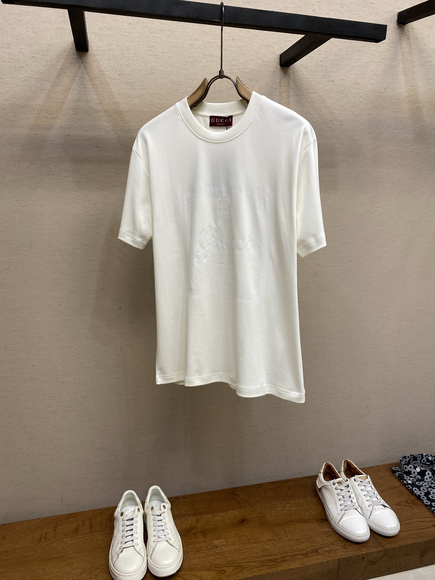 NO:685928,Gucci Buddha City printed round neck short sleeves. Available in black and apricot colors. Original purchase: 6.400; soft knitted cotton fabric, environmentally friendly elastic bright glue printing, round neck short sleeves, regular version, simple style, complete set of accessories #Soft knitted cotton fabric  This product uses 60-count single-yarn double-sided knitted cotton with a weight of 170g/㎡; the neckline and other parts are equipped with 32-count double-yarn ribbing. The high weight ensures a stable collar shape. 60-count is an extremely high count, which means the yarn is extremely fine, which directly gives the fabric an extraordinary delicate, silky and soft touch. Double-sided structure  The texture of the front and back of the fabric is consistent, uniform, thin and elastic. The weight of 170g is lightweight, ensuring the T-shirt is extremely light, breathable and drapey. It is almost invisible when worn, making it very suitable for the early spring season. The color of the fabric is soft and high-end, further enhancing the exquisite texture of the fabric.  # Environmentally Friendly Elastic Thick Plate Bright Glue The direct expression of printing collection elements uses the environmentally friendly elastic thick plate bright glue printing process to place such a three-dimensional, bright, and highly present slogan print on a simple knitted sweater. This is a high-end special printing technology. Thick plate means that the slurry is accumulated thickly, which can form an obvious three-dimensional effect; after the bright slurry is cured, the surface presents a high-gloss glossy effect; the slurry itself is elastic and can stretch with the fabric.  The special environmentally friendly elastic glossy slurry is thick-coated and transferred through the screen, and then cured at high temperature to create a brand slogan pattern with a significant 3D convex texture, mirror-like luster, and strong stretch resistance. The pattern area has obvious stiff convexity and smooth paint surface feel to the touch, which forms a strong contrast with the extremely soft fabric base and has a strong visual impact. # Round neck straight version  The straight and loose cut leaves margins in the armpits and side seams through three-dimensional cutting to achieve zero restriction of movement. The dropped shoulder design weakens the shoulder lines and enhances the casual atmosphere. Elastic molding strips are embedded in all seams, and the cuffs and hems adopt double-needle and double-thread seaming technology to ensure that the shape remains in its original state after multiple washes. Sizes XS-L,, gucci, T-shirt, tees, t-shirt,19860909Gucci 佛城印花圆领短袖 发售色系黑色、杏色 原6.400购买；柔软针织棉面料、环保弹力光亮胶浆印花、圆领短袖、常规版型、呈现简洁风格、全套辅料配备 # 柔软针织棉面料 本品采用60支单纱双面针织棉,克重为170g/㎡；领口等部位搭配32支双纱罗纹,高克重确保了领型稳定.60支属于极高支数,意味着纱线极细,这直接赋予了面料超凡的细腻、丝滑和柔软触感.双面结构面料正反面质感一致,质地均匀、轻薄且富有弹性.170g的克重属于轻量级,确保了T恤的极致轻盈、透气与悬垂感,穿着时几乎无感,非常适合早春季节.面料颜色泽柔和高级,进一步强化了面料的精致质感. # 环保弹力厚板光亮胶浆 印花典藏元素的直接表达采用环保弹力厚板光亮胶浆印花工艺,在简针织衫上放置如此立体、光亮、存在感极强的标语印花,这是一种高端的特殊印花技术.厚板指浆料堆积较厚,能形成明显的立体感；光亮浆料固化后表面呈现高光泽的亮面效果；浆料本身具有弹性,可随面料拉伸. 将特制的环保弹力光亮浆料通过网版厚涂转印,再经高温固化.创造出具有显著3D凸起质感、镜面般光泽且坚固耐拉伸的品牌标语图案.触感上图案区域有明显的硬挺凸起和光滑漆面感,与极其柔软的面料基底形成强烈对比,视觉冲击力强. # 圆领直筒版型 直筒宽松剪裁通过立体剪裁在腋下与侧缝预留余量,实现活动零束缚.落肩设计弱化肩部线条,强化休闲氛围.所有接缝内嵌弹力定型条,袖口及下摆采用双针双线锁边工艺,确保多次洗涤后版型依旧保持初始状态. 尺码XS-L,,gucci,T-shirt,tees，t-shirt,,Men's clothing