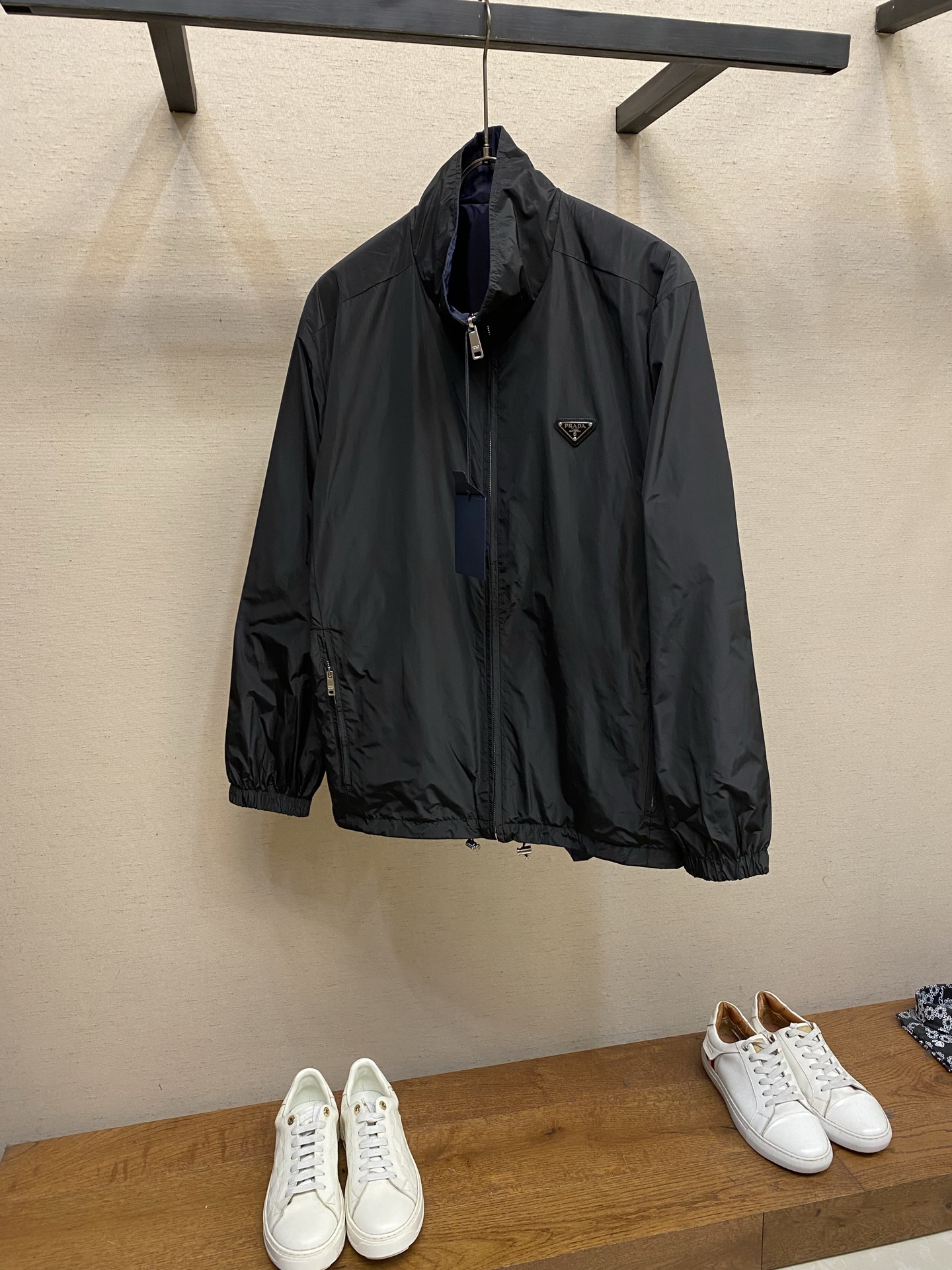 NO:746781,Prada Recycled Nylon Reversible Stand Collar Jacket Fabric Choices  Both sides are made of iconic nylon fabric. On the basis of the same performance as traditional nylon, the yarn breaking strength reaches 500N, which is far higher than ordinary nylon fabrics. The wear resistance is improved by 30, and it can cope with daily friction and stretching without stress. It weighs only 90g per square meter, making it light and burdenless to wear; the structure is stable and can be folded multiple times.  It can quickly return to flatness after use; it has excellent moisture absorption and quick-drying performance, and the water evaporation rate is 2 times faster than ordinary nylon, making it easy to take care of daily. One side is classic black, and the other side is deep 19860909Prada 再生尼龙双面穿立领夹克 面料选择 两面均采用标志性尼龙面料,与传统尼龙同等性能的基础上纱线断裂强度达500N,远超普通尼龙面料,耐磨损性能提升30,应对日常摩擦与拉伸无压力.每平方米重量仅90g,穿着轻盈无负担；结构稳定,多次折叠后仍能快速恢复平整；吸湿速干性能优异,水分蒸发速率比普通尼龙快2倍,日常打理便捷.一面为经典黑色,另一面为深邃藏青色,均采用哑光染色工艺,色泽均匀饱满,两面均可独立穿着,实现“一衣双搭”的实用价值. 工艺 所有缝份均采用0.4cm宽斜裁布条包裹,布条经纬向斜度精确至45°,确保拉伸时无褶皱.两层面料边缘对齐后折叠缝合,缝线完全隐藏于夹层,内外两面均无毛边外露,触感光滑细腻.在肩缝、袖窿等易受力部位,通过每10cm一处的“锚定点”手工固定,防止两层面料在穿着中相对滑动,确保版型稳定.使夹克即使双面穿着,仍能保持挺括轮廓,避免变形. 细节 立领采用双层尼龙面料,内层添加0.2mm薄型衬条,通过3道辑明线固定领型,领高控制在7cm左右,既贴合颈部曲线,又保持立体挺括,兼顾保暖与利落感. 尺码S-XL,,prada,jackets & coats,,Men's clothing