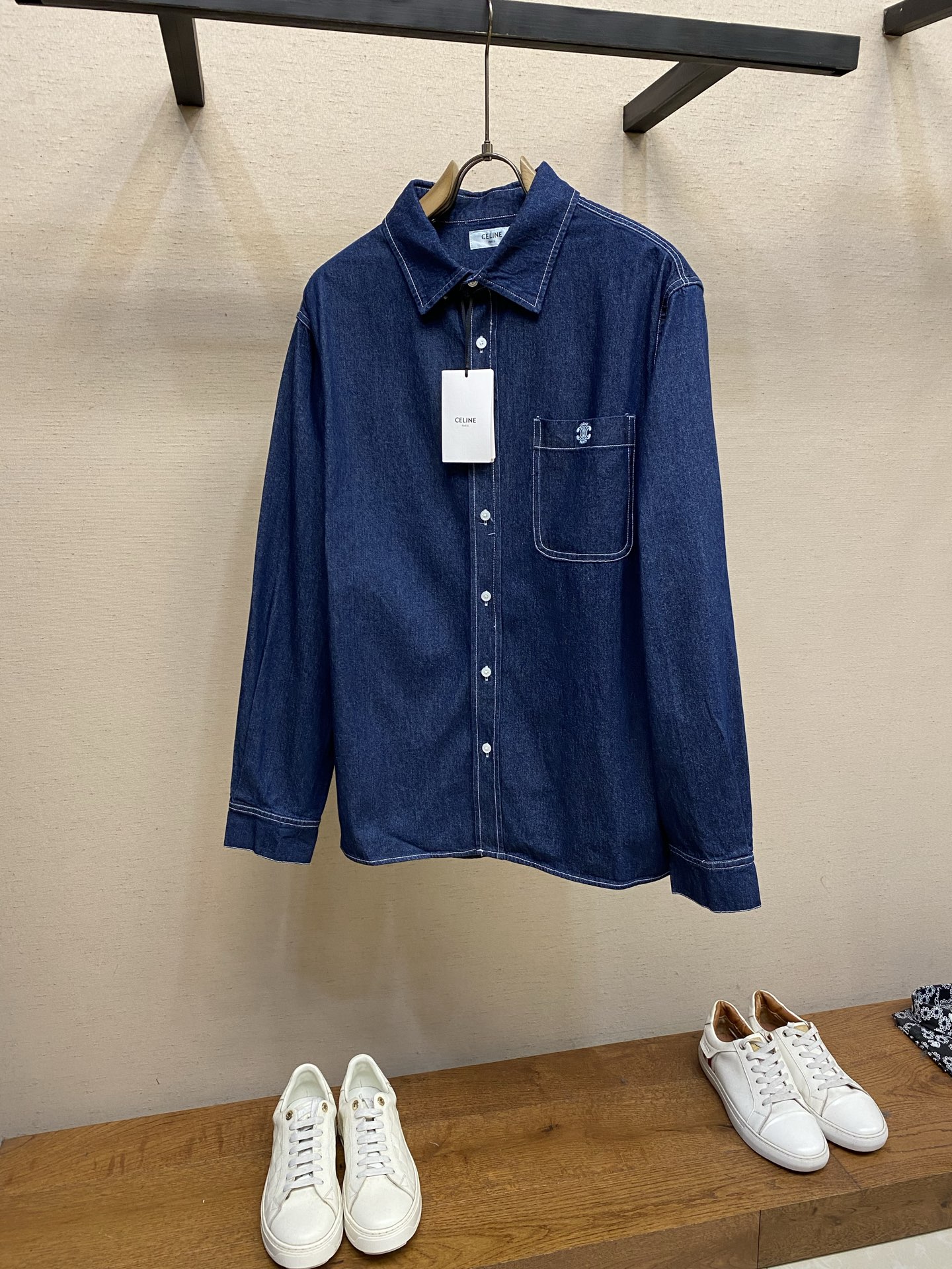 NO:746779,Celine embroidered denim shirt. Fabric selection. High-count cotton is selected and woven using traditional weaving technology. The yarn density reaches 12 ounces, which has a moderate sense of stiffness and softness. The cotton fiber is combed to remove short fiber impurities to ensure a fine and smooth surface of the fabric and reduce fluffing when wearing. The dark blue is dip-dyed with vegetable indigo dye to present a uniform and full color. Washing process  Natural biological enzymes are used to decompose floating colors and impurities on the surface of cotton fibers, making the fabric feel softer while retaining the original texture of the fabric to avoid excessive fading. At the same time, the water temperature and duration are strictly controlled during the washing process to ensure that the fabric shrinkage is controlled within 3%, ensuring that the size of the garment is stable and not easily deformed. Embroidery process  The embroidery machine outlines the logo with 0.3mm contrasting cotton thread, with fine and even stitches to ensure smooth and clear lines, forming a full three-dimensional texture that contrasts with the texture of the fabric. The embroidery area is about 2.5×2.5cm, and the edges are narrowed with 'overlock embroidery' to prevent the yarn from loosening and enhance the three-dimensional sense and durability of the pattern. The letter pattern in the logo is presented with micro flat embroidery, with a letter height of only 0.1cm, but clearly legible. Details  The 7 mother-of-pearl buttons on the front and the 3 buttons on the cuffs are fixed by hand stitching, and each button is reinforced with a cross knot to prevent it from falling off. The button holes are precisely polished to form a tight fit with the stitching, allowing smooth opening and closing without lag. Sizes S-XL,,celine,shirts,19860909Celine 饰刺绣牛仔衬衫 面料选择 甄选高支棉,采用传统梭织工艺织造,纱线密度达12盎司,兼具适度的挺括感与柔软度.棉纤维经过精梳处理,去除短纤杂质,确保面料表面细腻平整,减少穿着时的起毛现象.深蓝色通过植物靛蓝染料浸染,呈现均匀饱满的色泽. 水洗工艺 使用天然生物酵素分解棉纤维表面的浮色与杂质,使面料触感更柔软,同时保留面料的原始纹理,避免过度褪色.同时水洗过程中严格控制水温与时长,确保面料缩水率控制在百分之3以内,保证成衣尺寸稳定,不易变形. 绣花工艺 绣花机以0.3mm撞色棉线勾勒标志,针脚细密均匀,确保线条流畅清晰,形成饱满的立体肌理,与面料的质感形成对比.刺绣面积约2.5×2.5cm,边缘以“锁边绣”收针,防止纱线松散,同时增强图案的立体感与耐用性.标志中的字母图案以微型平绣呈现,字母高度仅0.1cm,却清晰可辨. 细节 前襟7枚珍珠母贝纽扣与袖口3枚纽扣均通过手工钉缝固定,每颗纽扣搭配十字花结加固,防止脱落.纽扣孔径经过精确打磨,与缝线形成紧密咬合,开合顺畅无卡顿. 尺码S-XL,,celine,shirts,,Men's clothing