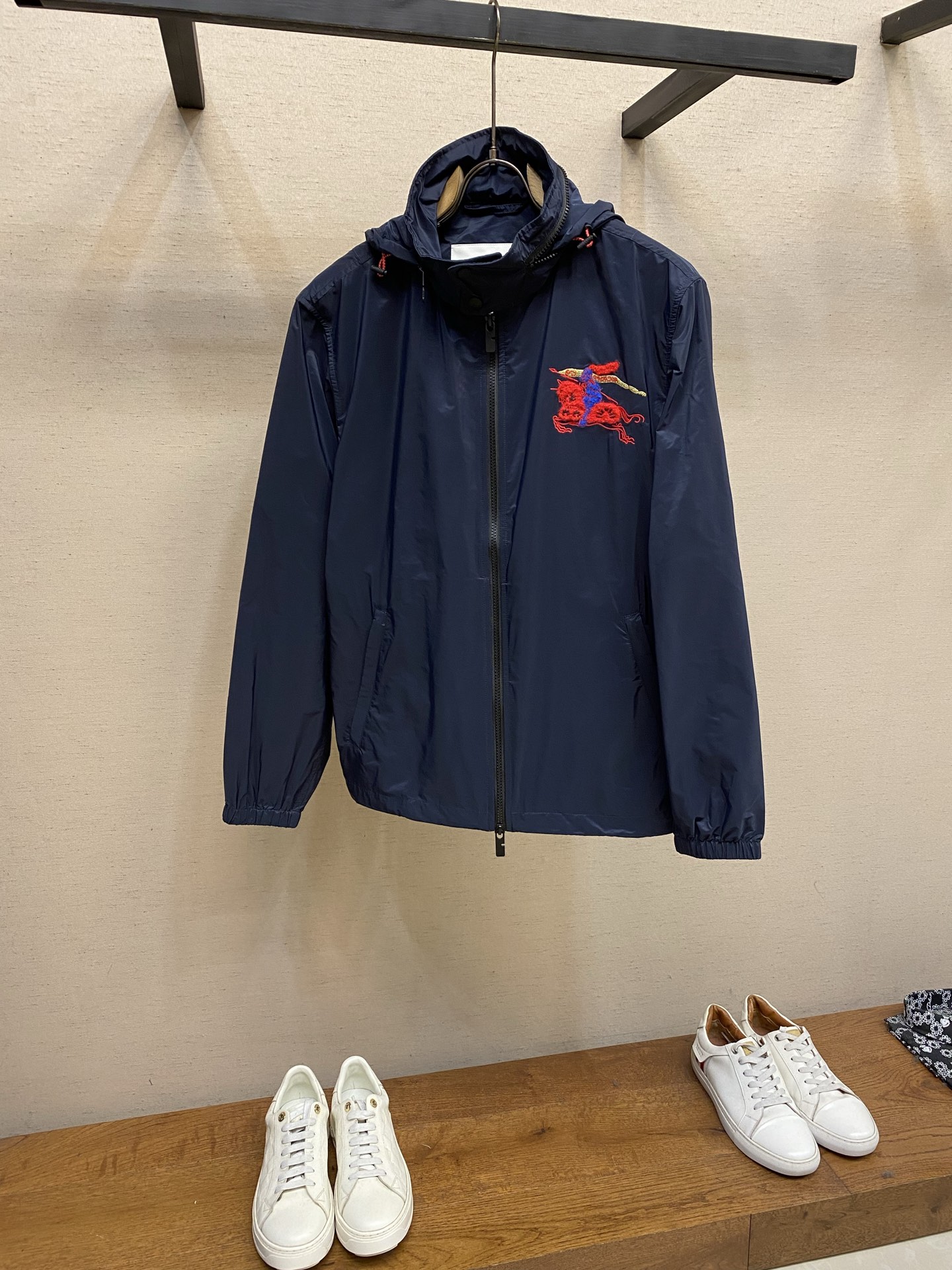 NO:746777,BBR War Horse Embroidered Hooded Jacket Fabric Selection The outer layer and lining are made of polyamide fabric. The plain weave high-density weaving process gives the fabric light and crisp characteristics. It weighs only 120g per square meter and is easy to wear. The high-density weaving of the fabric makes it waterproof to a certain extent, and water droplets can quickly condense and slide off after contact. The lining is made of polyamide plain cloth of the same color, which has a smooth touch, reduces friction with inner clothing, and improves wearing comfort. Embroidery process  The embroidery uses a combination of 'multi-color layered embroidery + towel embroidery', using red nylon thread to flatly embroider the dynamic outlines of the knight and horse. The stitch density reaches 8 stitches per centimeter to ensure smooth lines and capture the tension of the galloping horse. The horse body and knight's clothing are made of red and blue.  Filled with towel embroidery, a full texture is formed through the stacking of yarns, simulating the real touch of fur and fabric. The knight's cape is blended with golden metallic yarn, and chain embroidery is used to present an elegant and dynamic look, which contrasts sharply with the dark blue fabric and enhances the visual impact.  Details 1. The hood has a built-in concealable drawstring. The rope head is made of a red braided rope with a black plastic adjustment buckle, which supports the free adjustment of the size of the hat girth, taking into account practicality and style. 2. There is a set of drawstrings on both sides of the hem. The rope head and the hood rope are the same series of red braided ropes, which can freely adjust the waist tightness, windproof and warm; the cuffs are made of elastic flat ribs, which fit tightly around the wrist to prevent cold wind from entering while maintaining freedom of movement.  3. The pockets on both sides are designed with invisible zippers, and the zipper pulls echo the front zipper. The inside of the pocket is made of wear-resistant polyamide fabric, which significantly improves its service life. Sizes S-XL,,jackets & coats,hats,19860909BBR 战马绣花连帽夹克 面料选择 外层与内衬均采用聚酰胺面料,通过平纹高密度织造工艺,赋予面料轻薄挺括的特性,每平方米重量仅120g,穿着无负担.面料的高密度编织使其具有一定的防水性,水滴接触后可迅速凝结滑落.内衬采用同色系聚酰胺平布,触感光滑,减少与内搭衣物的摩擦,提升穿着舒适度. 绣花工艺 刺绣采用“多色分层绣+毛巾绣”复合,以红色锦纶线平绣骑士与骏马的动态轮廓,针脚密度达每厘米8针,确保线条流畅,捕捉马匹奔腾的张力.马身与骑士服饰部分采用红色与蓝色毛巾绣填充,通过纱线的堆叠形成饱满的肌理感,模拟皮毛与织物的真实触感.骑士披风处融入金色金属感纱线,以链式绣呈现飘逸动态,与深蓝色面料形成鲜明对比,增强视觉冲击力. 细节 1连帽内置可隐藏式抽绳,绳头采用红色编织绳搭配黑色塑胶调节扣,支持自由调节帽围大小,兼顾实用性与造型感. 2下摆两侧各设一组抽绳,绳头与帽绳同系列红色编织绳,可自由调节腰围松紧,防风保暖；袖口采用弹性扁牛筋,紧密贴合手腕,防止冷风灌入,同时保持活动自如. 3两侧口袋采用隐形拉链设计,拉链头与前襟拉链呼应,口袋内部采用耐磨聚酰胺面料,使用寿命得到显著提升. 尺码S-XL,,jackets & coats,hats,,Men's clothing