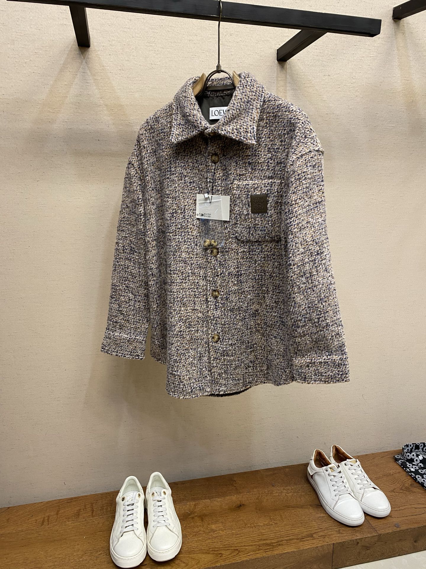 NO:746775,Loewe wool blend shirt jacket fabric options  Using carefully proportioned blended fabrics, wool provides natural warmth and a crisp silhouette, mohair gives the fabric a fine and fluffy velvety feel, and a small amount of nylon is added to enhance wear resistance and wrinkle resistance. The three are combined to create an ideal thickness of medium weight, taking into account both temperature and lightness. Through the 'double-sided sanding' process, the fabric  The surface presents a rich short-pile texture, which feels as soft and skin-friendly as cashmere, while retaining the sinewy feel of wool blending. The micro-check pattern is based on sand beige, interwoven with gray, brown, and blue yarns, and is woven through a yarn-dyed process. The micro-check pattern is uniform in size, delicate and unobtrusive, presenting a low-key retro charm.  Process: The fabric goes through 3 sanding processes to ensure uniform pile length (about 0.3mm) and no obvious pilling. After sanding, it undergoes 'low temperature pre-shrinking' treatment to control the shrinkage within 2 to ensure stable size of the garment. Details  1. The collar is made of double-layer fabric and is three-dimensionally cut. The collar tip angle is controlled at 80°. The collar lining is fixed by hand sewing to ensure that it is stiff and not easy to deform. The length of the collar is set to 2CM below the standard waistline, which not only retains the neatness of the shirt, but also can be worn as a jacket.  2. The front buttons are horn buttons, with a unique amber texture on the surface. The button holes are sewn with 'hand-made keyhole' technology, and each hole is finely seamed to ensure durability. There are 2 horn buttons of the same series on the cuffs, which can be adjusted for tightness and fit the wrist line. Customized leather label  It is made of calfskin, with a thickness of only 0.8mm, soft and elastic, and is slightly oiled to give it a warm matte luster. The Anagram pattern is embossed on the leather surface through precision imprinting at 120°C high temperature and 8kg/cm pressure, with a pattern depth of 0.2mm, clear and smooth lines, and no burrs on the edges. After imprinting, it is hand-polished to create a natural contrast between light and dark on the leather surface and enhance the three-dimensional sense of the pattern. Sizes S-XL,, loewe, jackets &  coats,shirts,cowhide,19860909Loewe 羊毛混纺衬衫式外套 面料选择 采用精心配比的混纺面料,羊毛提供天然保暖与挺括廓形,马海毛赋予面料细腻蓬松的绒毛感,少量锦纶的喂入则增强耐磨性与抗皱性,三者融合打造中克重的理想厚度,兼顾温度与轻盈.通过“双面磨毛”工艺处理,面料表面呈现丰盈的短绒毛肌理,触感如羊绒般柔软亲肤,同时保留羊毛混纺的筋骨感.微型格纹图案以沙米色为基底,交织灰、棕、蓝三色纱线,通过色织工艺织就,微型格纹尺寸统一,细腻而不张扬,呈现低调的复古韵味. 工艺 面料经过3道磨毛工序,确保绒毛长度均匀（约0.3mm）,无明显起球现象.磨毛后进行“低温预缩”处理,将缩水率控制在2以内,保证成衣尺寸稳定. 细节 1衣领采用双层面料立体剪裁,领尖角度控制在80°,通过手工纳缝固定领衬,确保挺括不易变形.衣长设定为标准腰线以下2CM,既保留衬衫的利落感,又可作为外套单穿. 2前襟纽扣采用牛角扣,表面呈现独特的琥珀色纹理.纽扣孔以“手工锁眼”工艺缝制,每孔经细密锁边,确保耐用性.袖口处设2颗同系列牛角扣,可调节松紧,贴合手腕线条. 定制皮标 采用小牛皮,厚度仅0.8mm,质地柔软且富有弹性,经过轻微油润处理,呈现温润的哑光光泽.通过120℃高温、8kg/cm压力的精密压印,将Anagram图案压印于皮革表面,图案深度达0.2mm,线条清晰流畅,边缘无毛刺.压印后经过手工打磨,使皮革表面形成自然的明暗对比,增强图案的立体感. 尺码S-XL,,loewe,jackets & coats,shirts,cowhide,,Men's clothing