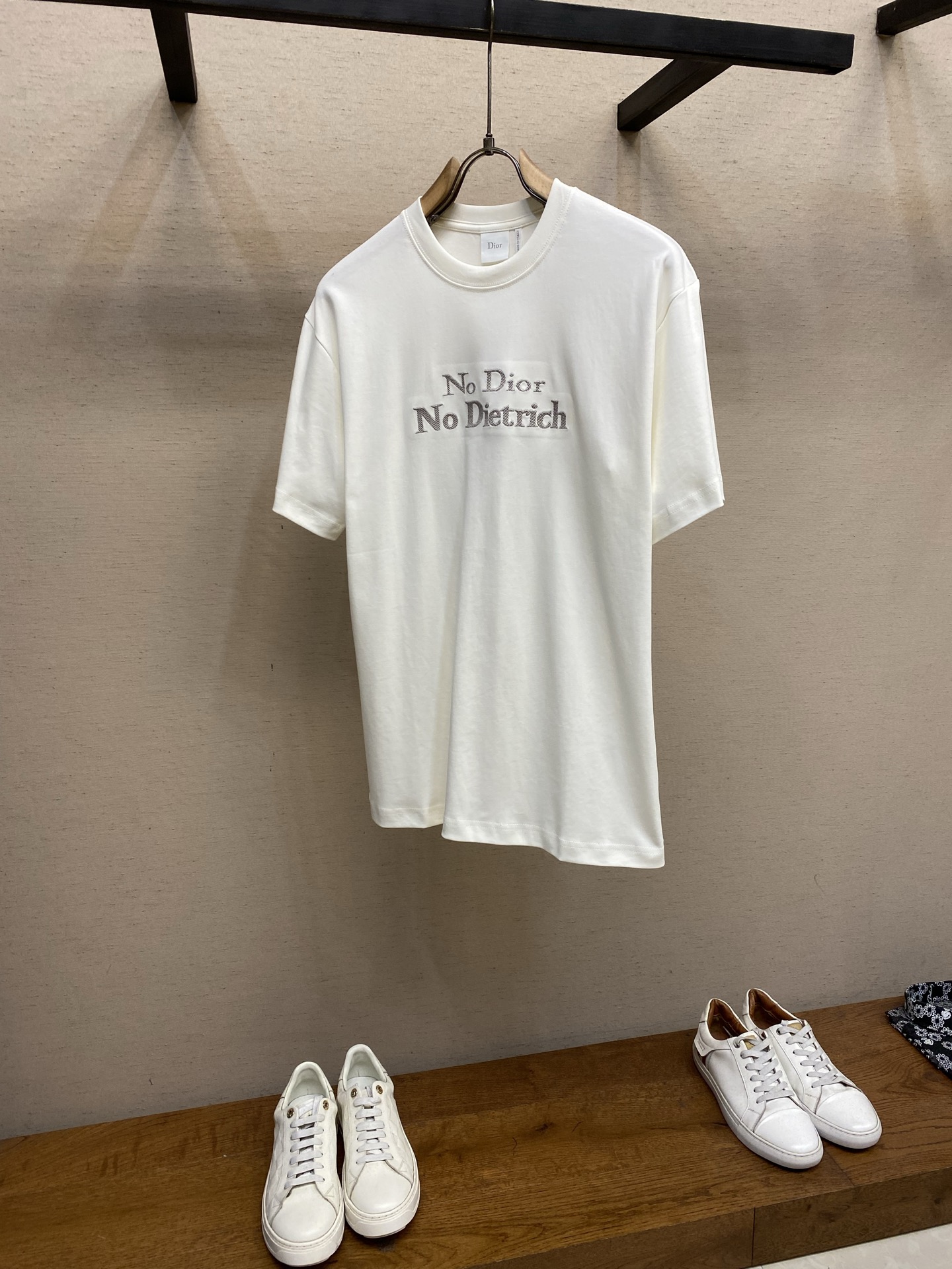 NO:761683,PDior statement embroidered round neck short sleeves. Available in apricot white and black. Original purchase; single yarn double-sided knitted cotton fabric, twill needle embroidery, regular round neck version, new accessories # single yarn double-sided knitted cotton fabric  This product is made of 60-count single-yarn double-sided knitted cotton with a weight of 170g/㎡; it is paired with a 32-count double-yarn high-weight rib with a weight of 300g/㎡. The neckline provides crucial strong support for the ultra-thin and delicate body, ensuring that the neckline remains stiff for a long time.  60 is an ultra-high count, which means that the yarn is extremely fine, giving the fabric an unparalleled delicate, silky and soft touch. The double-sided structure makes the front and back of the fabric have the same texture, uniform texture, light and elastic. The weight of 170g is light to medium, ensuring the T-shirt is extremely light, breathable and has excellent drape. The white base is pure and high-end. # Twill needle embroidery process  Straight-line embroidery in which stitches are closely connected and evenly arranged is a classic technique for outlining clear outlines and lines. Twill processing means that the arrangement direction of embroidery stitches is not the usual horizontal or vertical direction, but diagonal parallel lines at a specific angle.  Specially selected embroidery threads are used to accurately embroider the text with high-density stitches according to the preset diagonal trajectory, creating text lines with a unique texture direction and visual dynamics. The diagonal stitches will produce subtle light and dark changes under the light, enhancing the three-dimensional sense and artistic expression of the text, making it not just text, but more like a micro-artwork with texture, forming a textural contrast with the smooth and delicate cotton base. # Regular round neck style  Regular fit tailoring adopts three-dimensional shoulder line and straight waist design, and a transparent stabilizing film is implanted at the corresponding position of the embroidery to completely solve the shrinkage problem of ultra-thin fabric embroidery. The neckline adopts double hemming technology, and memory elastic yarn is embedded inside. All seams are implemented with three-needle five-thread interlock seams, and the seams are laser cut and hot-melt hemmed to achieve a zero-touch wearing experience. Sizes XS-L, dior, T-shirt, tees, t-shirt,19860909PDior 宣言刺绣圆领短袖 发售色系杏白、黑色 原购买；单纱双面针织纯棉面料、斜纹挨针刺绣、常规圆领版型、新款辅料配备 # 单纱双面针织纯棉面料 本品采用60支单纱双面针织棉,克重为170g/㎡；搭配32支双纱高克重罗纹,克重为300g/㎡.领口为超薄细腻的衣身提供了至关重要的强力支撑,确保领口长期挺括. 60支属于超高支数,意味着纱线极细,赋予面料无与伦比的细腻、丝滑和柔软触感.双面结构使面料正反面质感一致,质地均匀、轻薄且富有弹性.170g的克重属于轻薄至中等,确保了T恤的极致轻盈、透气与优良的悬垂感.白色基底纯净而高级. # 斜纹挨针刺绣工艺 挨针刺绣针脚紧密相连、排列均匀的直线绣,是勾勒清晰轮廓和线条的经典技法.斜纹处理指刺绣针脚的排列方向并非通常的水平或垂直,而是呈特定的角度的斜向平行线. 使用特选的绣线,按照预设的斜向轨迹,以高密度针脚精准绣出文字,创造出具有独特纹理方向感和视觉动感的文字线条.斜纹针脚在光线下会产生微妙的明暗变化,增强了文字的立体感和艺术表现力,使其不仅仅是文字,更像是一件有肌理的微型艺术品,与光滑细腻的棉质基底形成质感对比. # 常规圆领版型 常规合身剪裁通过立体肩线与直腰设计,在刺绣对应位置植入透明稳定膜,彻底解决超薄面料刺绣收缩难题.领口采用双重包边工艺,内部嵌入记忆弹力纱线.所有接缝实施三针五线绷缝,缝份经激光切割与热熔包边,实现零触感穿着体验. 尺码XS-L,,dior,T-shirt,tees，t-shirt,,Men's clothing