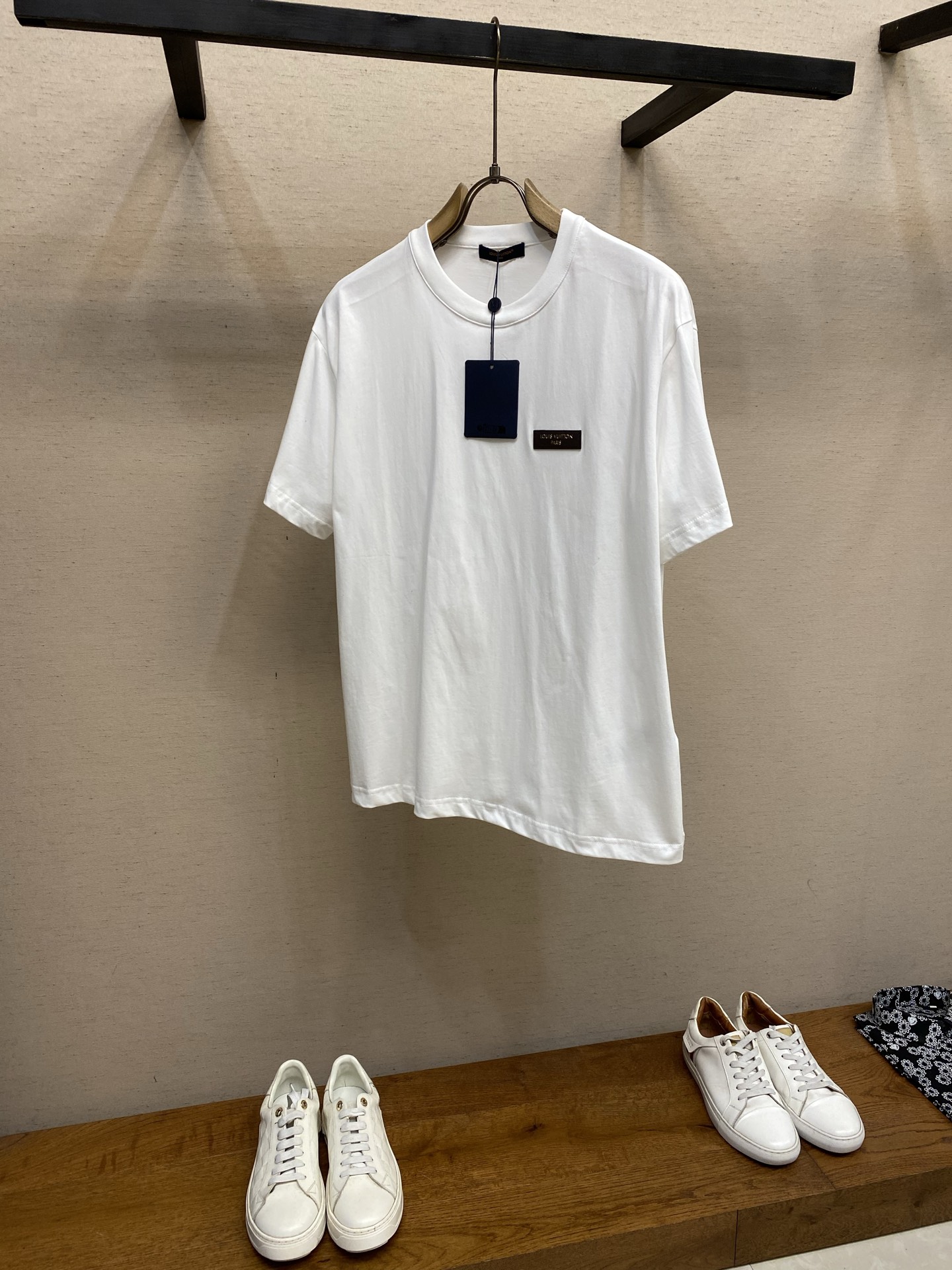 NO:828798,V, white tea leather round neck short sleeves. Original purchase; soft cotton knitted fabric, gold stamped leather patch on the chest, slim fit, full set of accessories # soft cotton knitted fabric Made of 24-count special-spun compact cotton, 185g/㎡; paired with 32-count 1×1 rib, 95 cotton 5-alen, 340g/㎡. The fabric is a medium-thick knit that is both stiff and comfortable. The fabric is tentered and shaped by a high-temperature setting machine, and the warp is made through tension control. The weft yarn is restored to straightness. The compact spinning technology makes the fibers arranged parallel, hairiness is significantly reduced, and the surface is smooth and clean. The collar adopts 32-count 1×1 ribs. The weaving structure makes the ribs dense, and the spandex component ensures that it can still fit the neck tightly after repeated wearing and taking off, and is not easy to loosen and deform. # The hot stamping leather patch on the chest is the core craftsmanship of this T-shirt. The patch is made of the same quality leather, and the brand logo is embossed on the surface through a hot stamping process - a heated metal mold is used to transfer the gold foil to the leather surface to form a hot stamping lettering with strong gloss and sharp edges. The patch and fabric are fixed using precision sewing technology, and the sewing method is reinforced with fine stitches along the edge of the patch, which not only improves the firmness but also adds decorative stitches. # The silhouette characteristics of the slim fit are slim fit design, which is a cut that fits the curve of the body but is not tight. The shoulder line accurately falls on the acromion point, the body is slightly tapered, the sleeves are standard short sleeves, and the sleeve fat is moderately narrowed. The stiffness of the fabric supports the structural sense of the slim fit - it not only fits the body shape and outlines the outline, but does not cause tightness or discomfort due to being too tight. Sizes XS-L,, T-shirt, tees, t-shirt,19860909V,白茶皮革圆领短袖 原购买；柔软棉质针织面料、胸前点缀烫金皮革贴饰、修身版型、全套辅料配备 # 柔软棉质针织面料 采用24支特纺紧密棉,185g/㎡；搭配32支1×1罗纹,95棉5安伦,340g/㎡.面料属于兼具挺括与舒适的中厚型针织,面料经高温定型机进行拉幅定形,通过张力控制使经纬纱恢复平直.紧密纺技术使纤维排列平行、毛羽显著减少,表面光洁平滑.领型采用32支1×1罗纹,编织结构使罗纹致密,氨纶成分确保反复穿脱后仍能紧密贴合颈部,不易松垮变形. # 胸前点缀烫金皮革贴饰 胸前点缀的烫金皮革贴饰是这款T恤的核心工艺.贴饰选用同品质皮革,表面通过烫金工艺压印品牌标识——利用加热的金属模具将金色箔纸转移至皮革表面,形成光泽感强、边缘锐利的烫金字样.贴饰与面料的固定采用精密车缝工艺,车缝法则沿贴饰边缘以细密针脚加固,既提升牢固度,又增添装饰性线迹. # 修身版型的廓形特点 采用修身版型设计,属于贴合身体曲线但不紧绷的剪裁.肩线精准落在肩峰点,衣身呈微锥形收窄,袖型为标准短袖且袖肥适度收窄.面料的挺括性支撑了修身版型的结构感——既贴合身形勾勒轮廓,又不会因过于紧身而产生勒痕或不适. 尺码XS-L,,T-shirt,tees，t-shirt,,Men's clothing